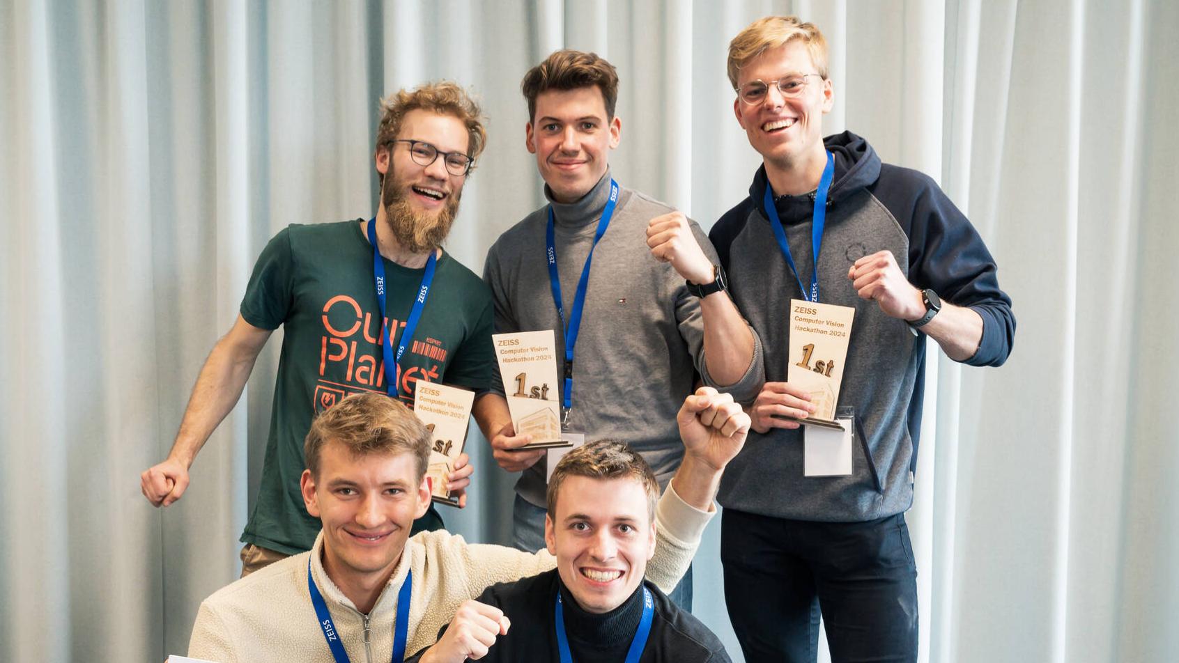 Ein Gruppenfoto vom Gewinnerteam des ZEISS Computer Vision Hackathon 2024. Zwei der fünf Teilnehmer halten einen überdimensionalen Scheck.