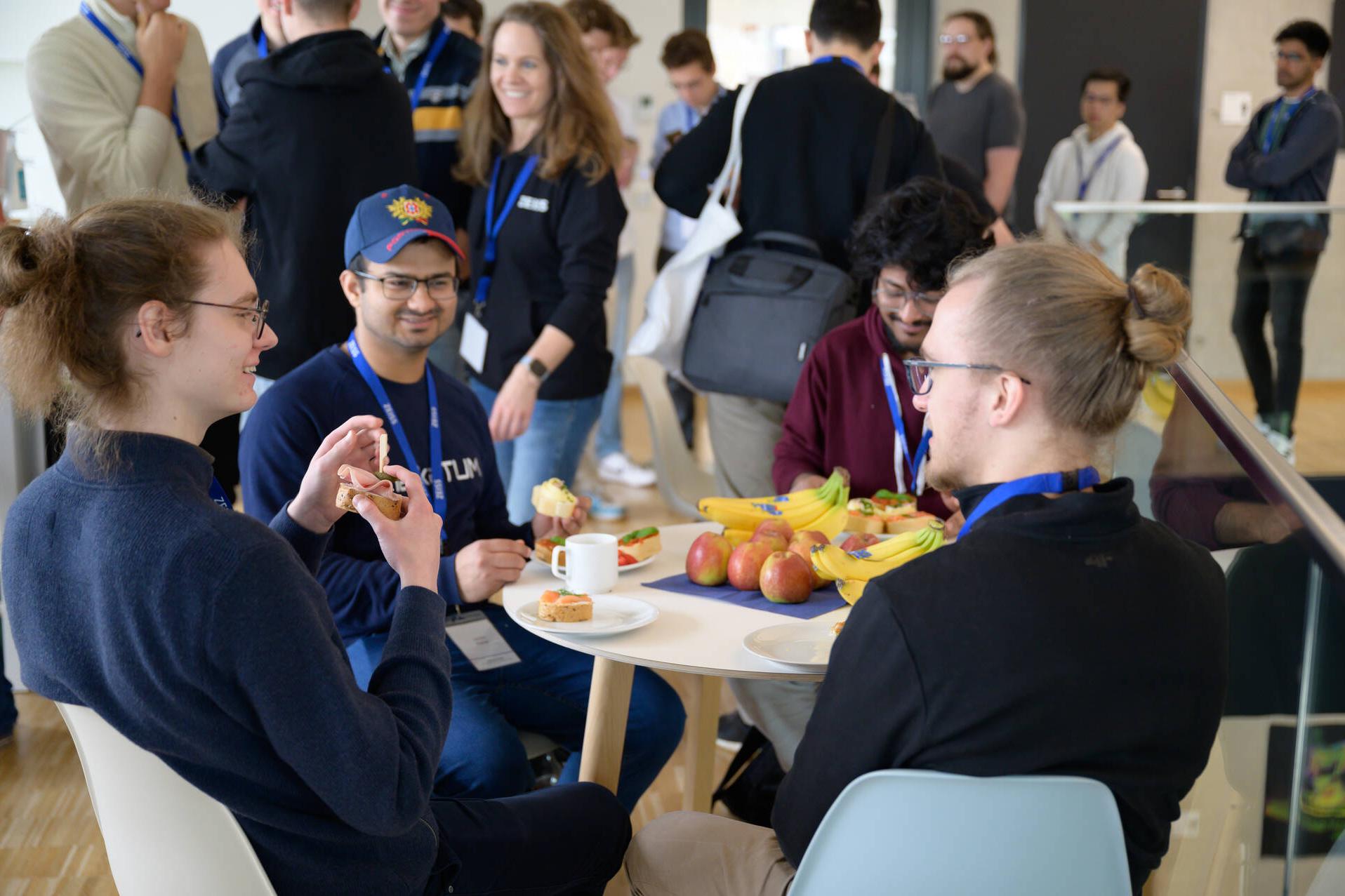 Vier Hackathon Teilnehmer sitzen an einem Tisch mit Kaffee, Snacks und Obst.