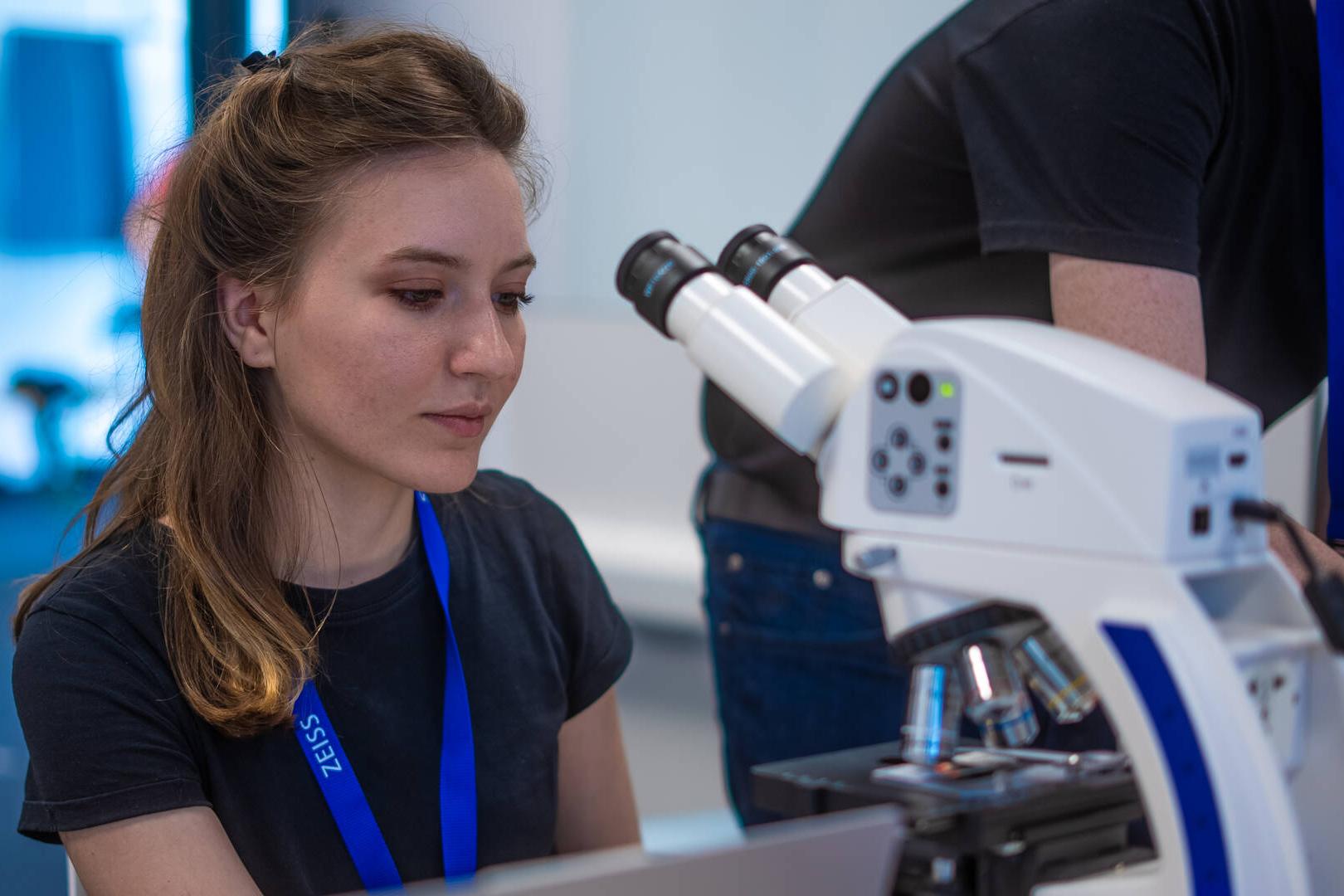 Ein Teilnehmer des ZEISS Computer Vision Hackathon 2024 sitzt an einem Tisch vor einem Mikroskop.