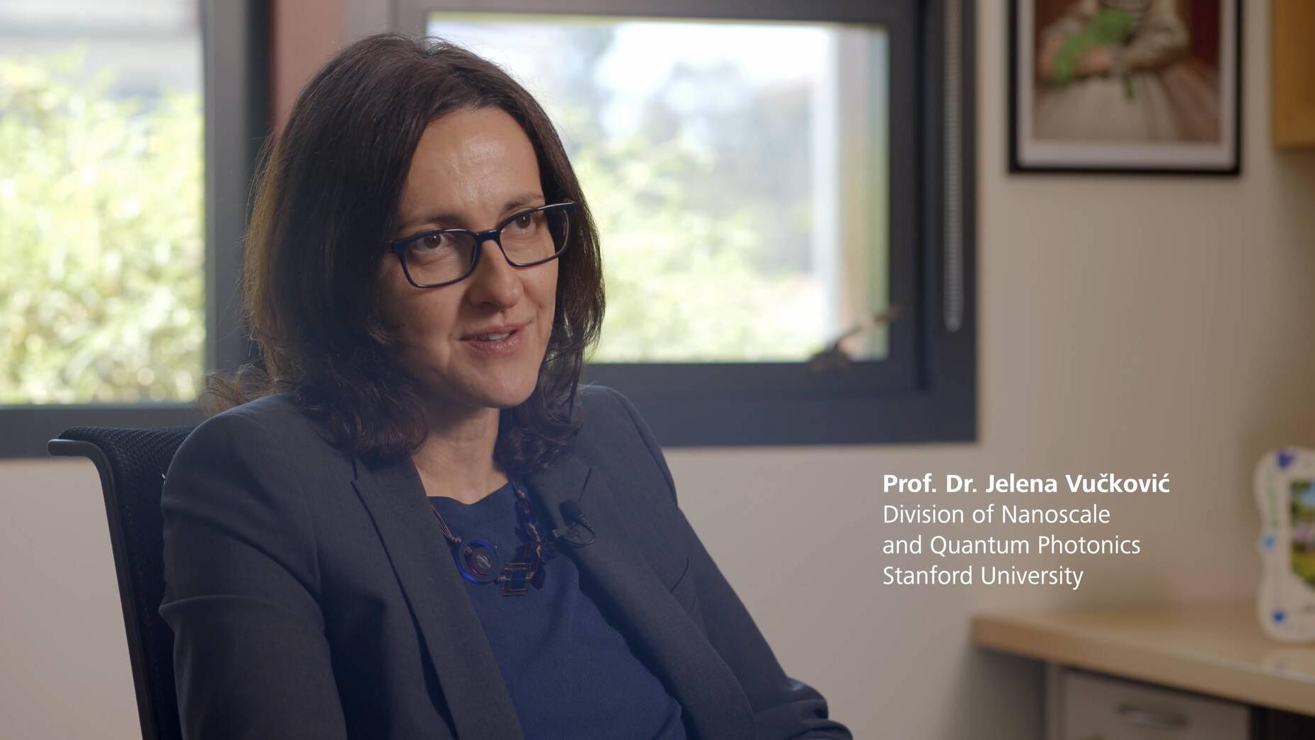 ZEISS Research Award Gewinnerin 2025: Prof. Dr. Jelena Vučković sitzt in ihrem Büro, trägt eine dunkelblaue Bluse und einen marineblauen Blazer. Sie hat schulterlanges dunkelbraunes Haar, trägt eine rechteckige Brille und blickt schräg an der Kamera vorbei.