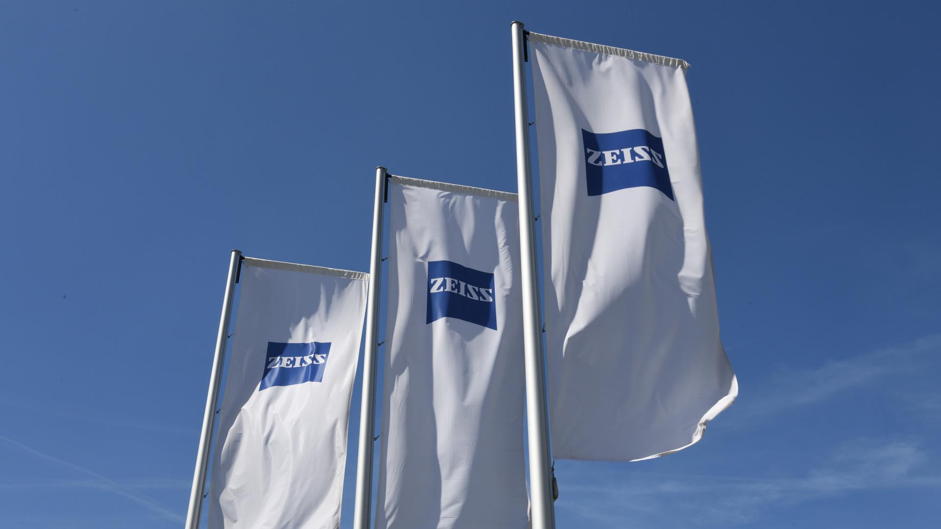 Drei weiße Fahren mit ZEISS Logo vor blauem Himmel