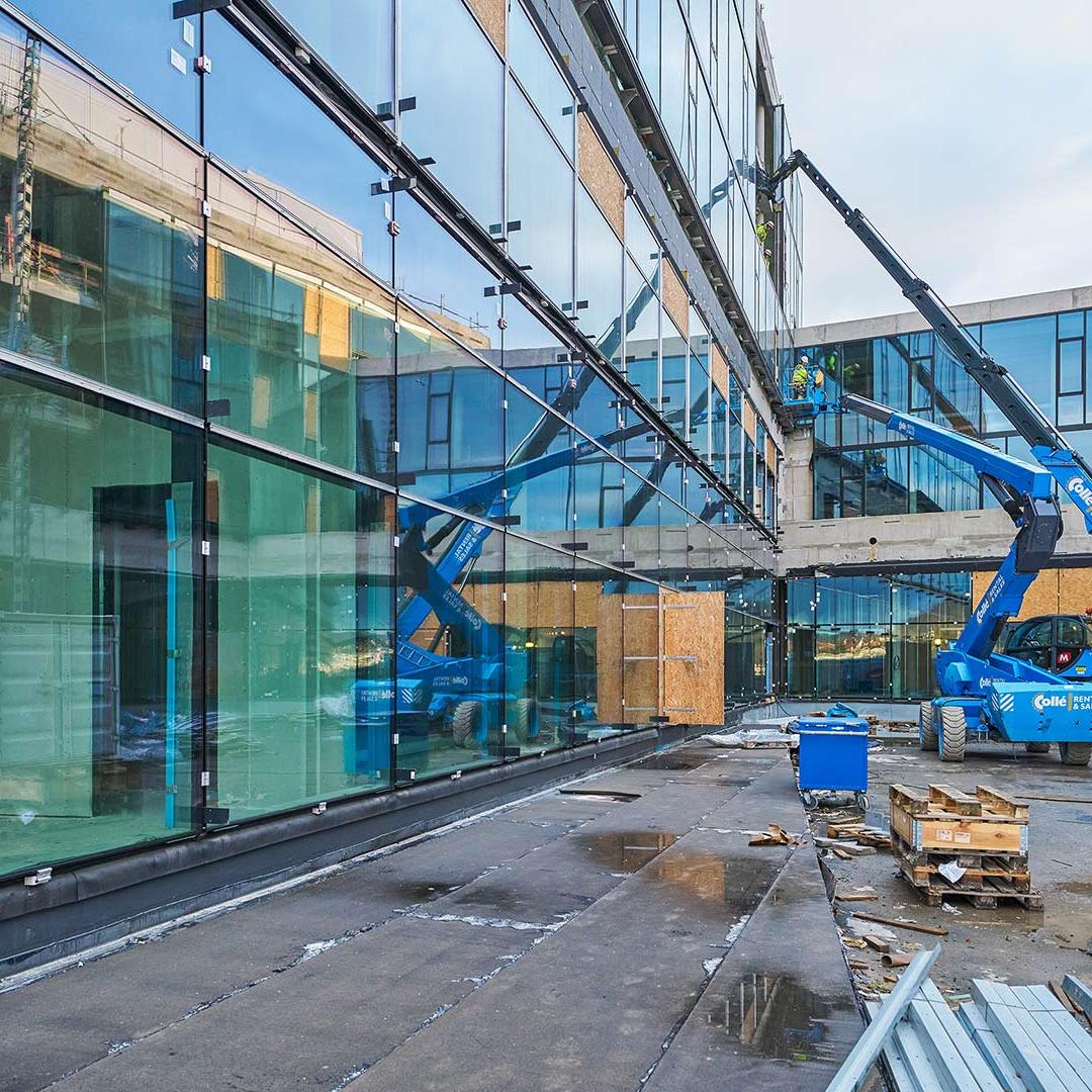 Blaue Hebebühne vor Glasfassade eines modernen Gebäudes mit reflektierenden Fenstern.