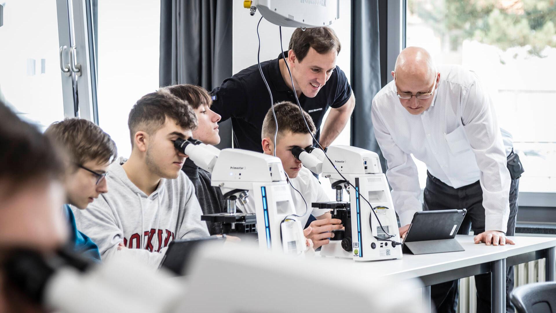 Schüler und Schülerinnen arbeiten an Mikroskopen im Unterrichtsraum