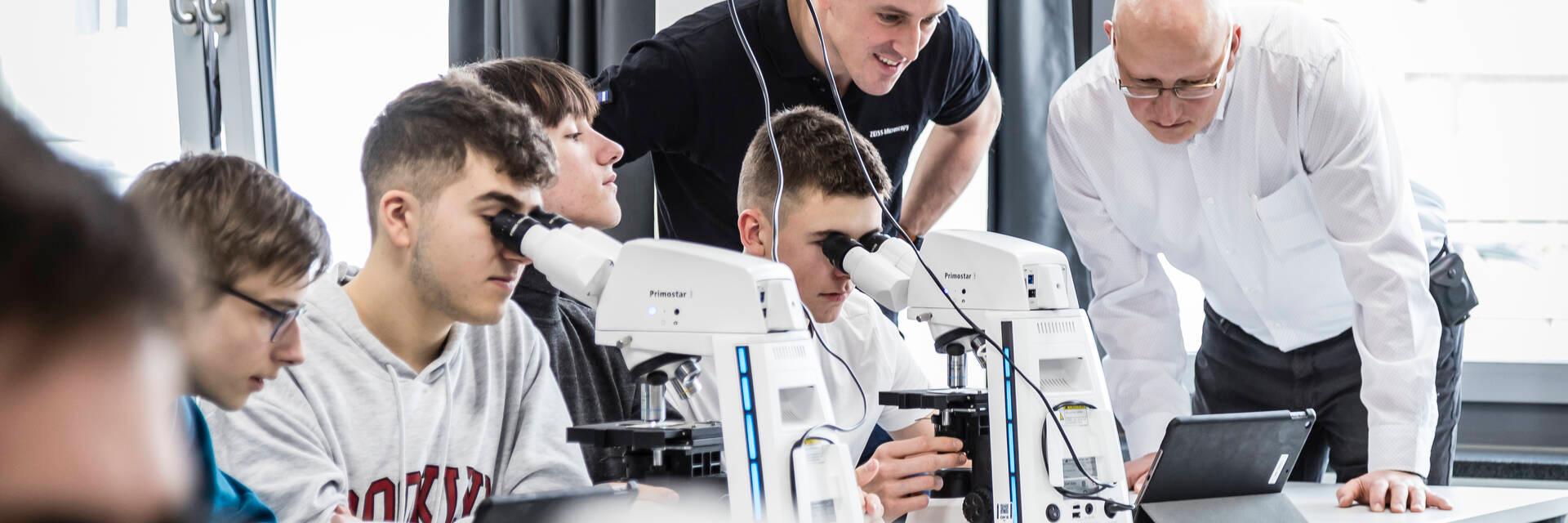 Schüler und Schülerinnen arbeiten an Mikroskopen im Unterrichtsraum