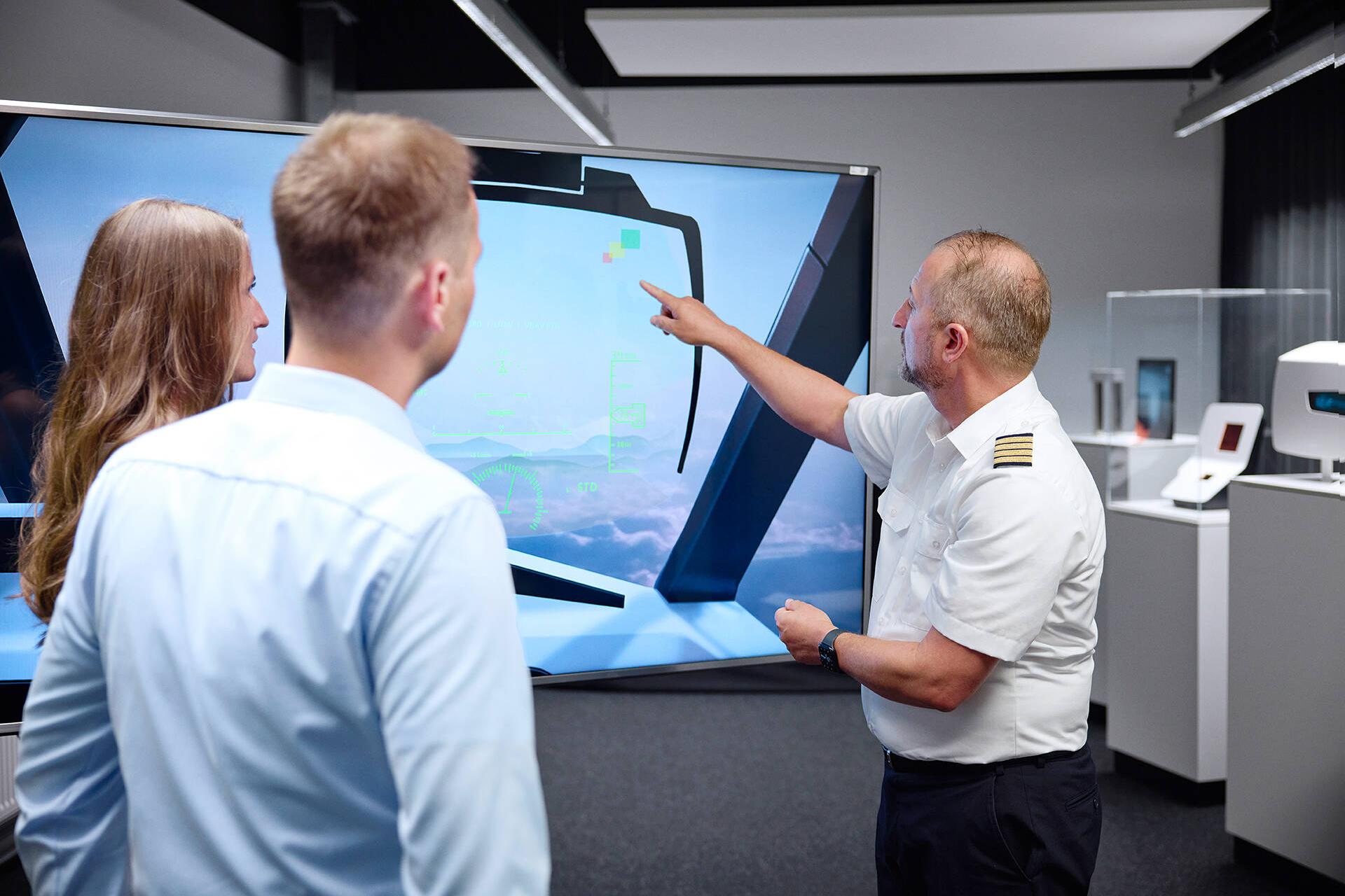 Berufspilot Tino Janke zeigt Linda und Dennis das Modell eines Head-Up-Displays, bei dem dank Augmented Reality wichtige Informationen direkt ins Sichtfeld projiziert werden.