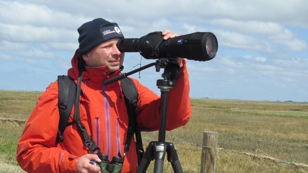 Ortinthologe in roter Jacke beobachtet Vögel