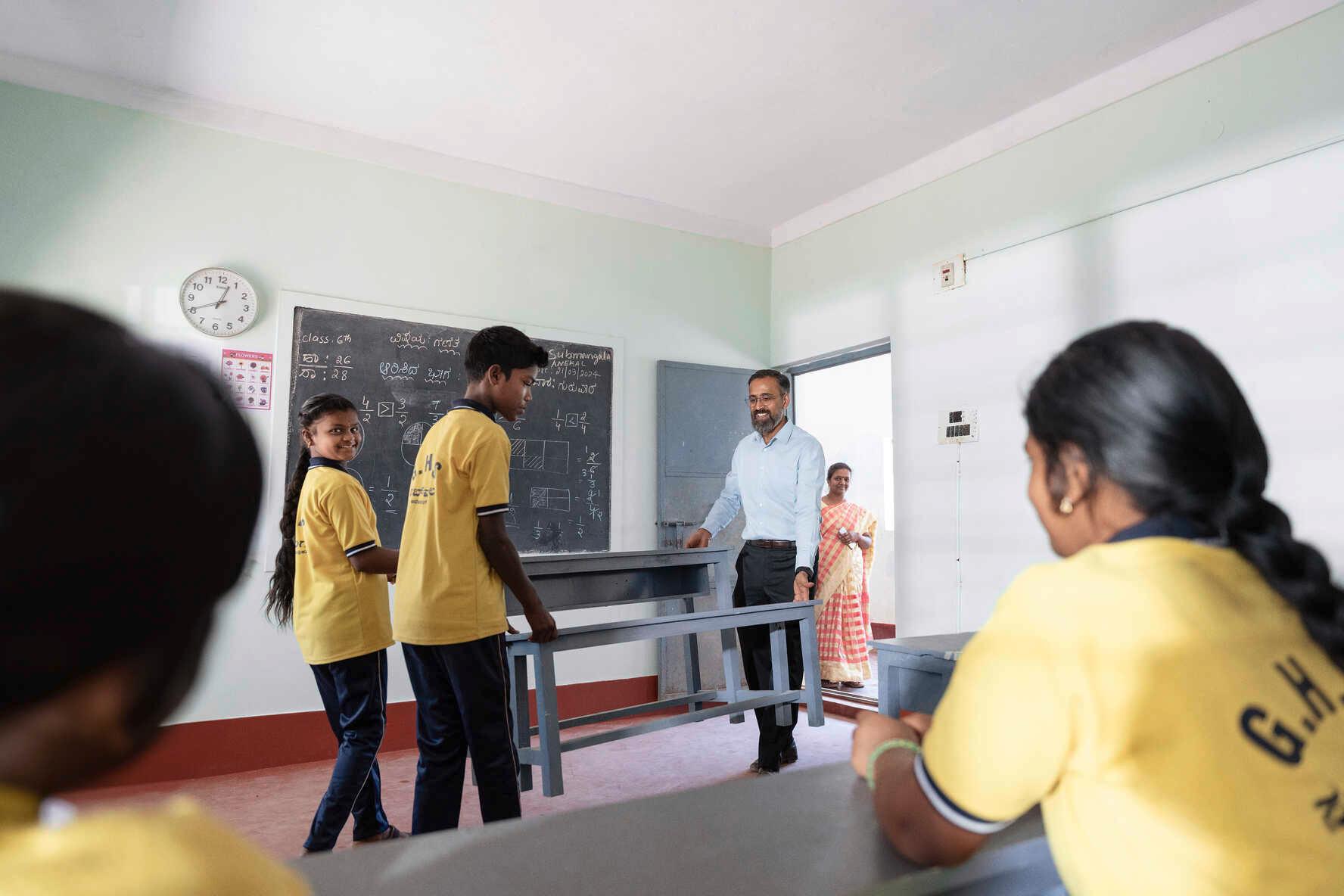 Schüler helfen Manoj Sharma, neue Bänke in ein Klassenzimmer zu tragen