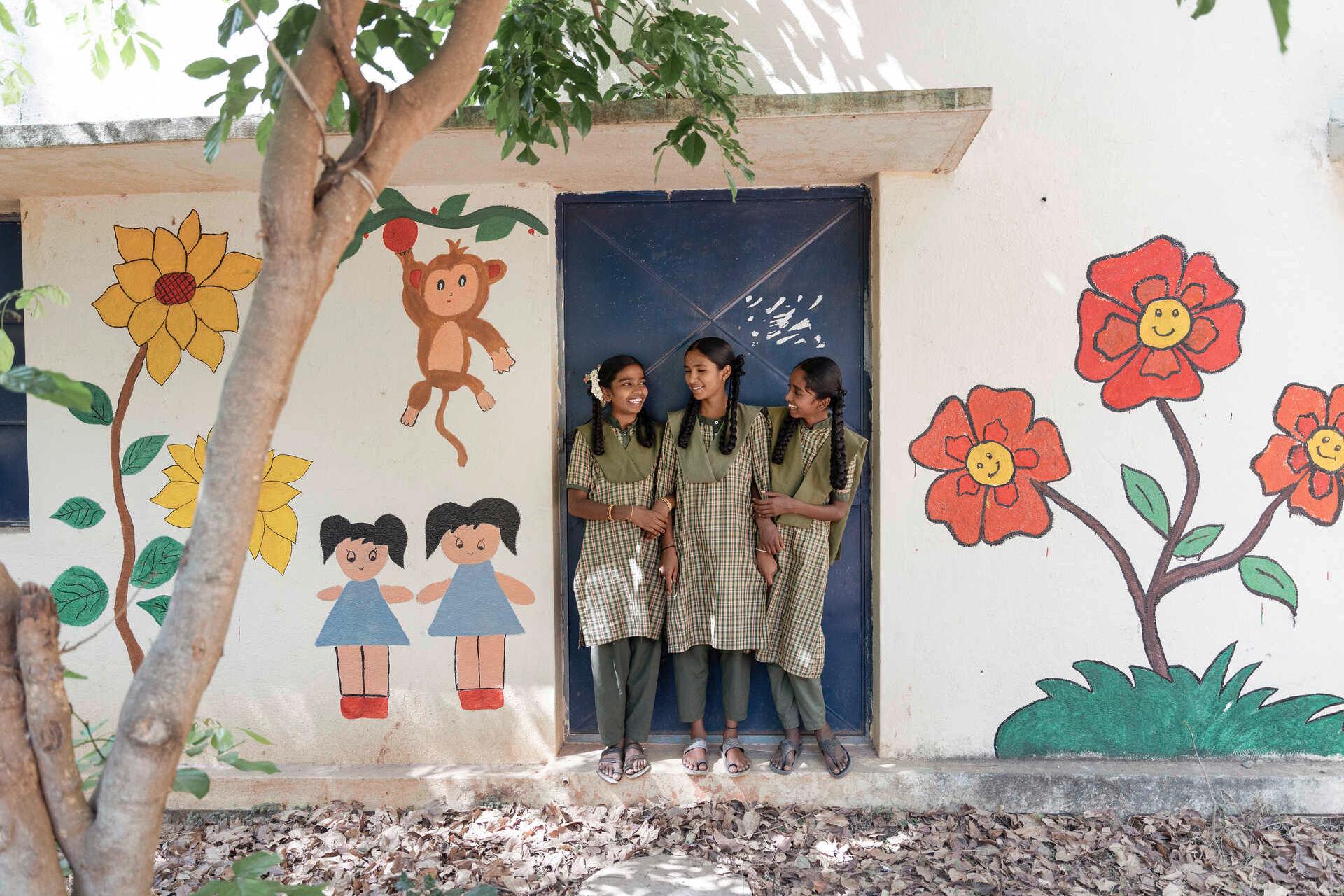 Drei Kinder stehen in einer Tür eines bunt bemalten Schulgebäudes