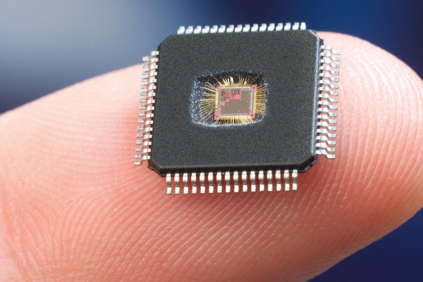 Eine Hand hält einen Mikrochip in die Kamera.