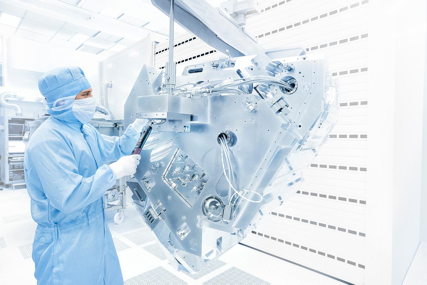 ZEISS-Mitarbeiter in hellblauer Reinraumbekleidung steht neben Maschinen für die EUV-Technologie.