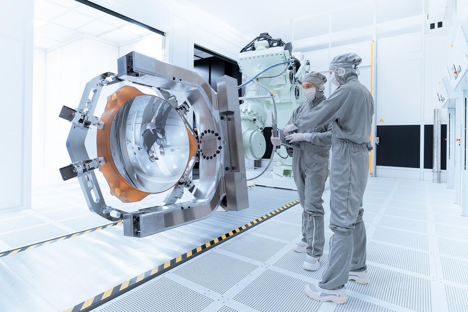 Zwei ZEISS-Mitarbeiter stehen neben der Maschine für die High-NA-EUV-Lithographie zur Fertigung von Mikrochips.