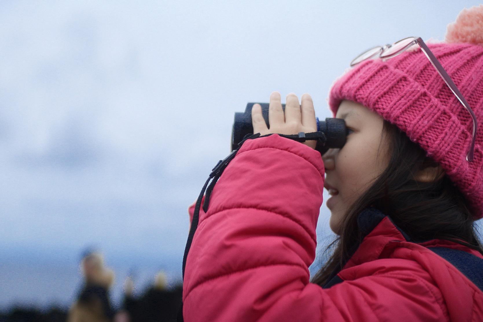 Schülerin schaut durch ein ZEISS Fernglas