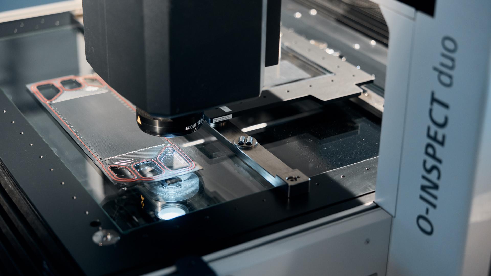 Nahaufnahme eines ZEISS O-INSPECT duo Geräts, das ein Metallteil auf seiner Messplattform prüft.