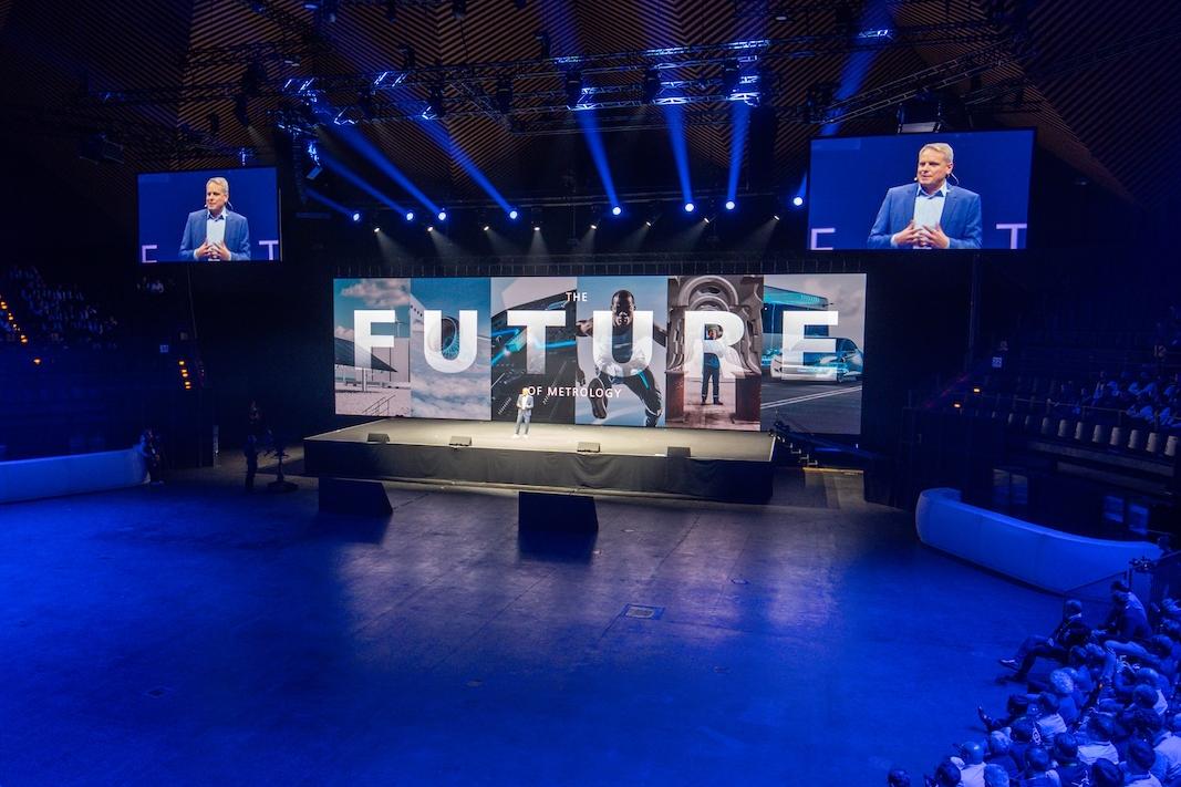 A large audience watches a ZEISS event in a circular auditorium with a prominent stage displaying the word "FUTURE" and speakers under dramatic blue lighting.
