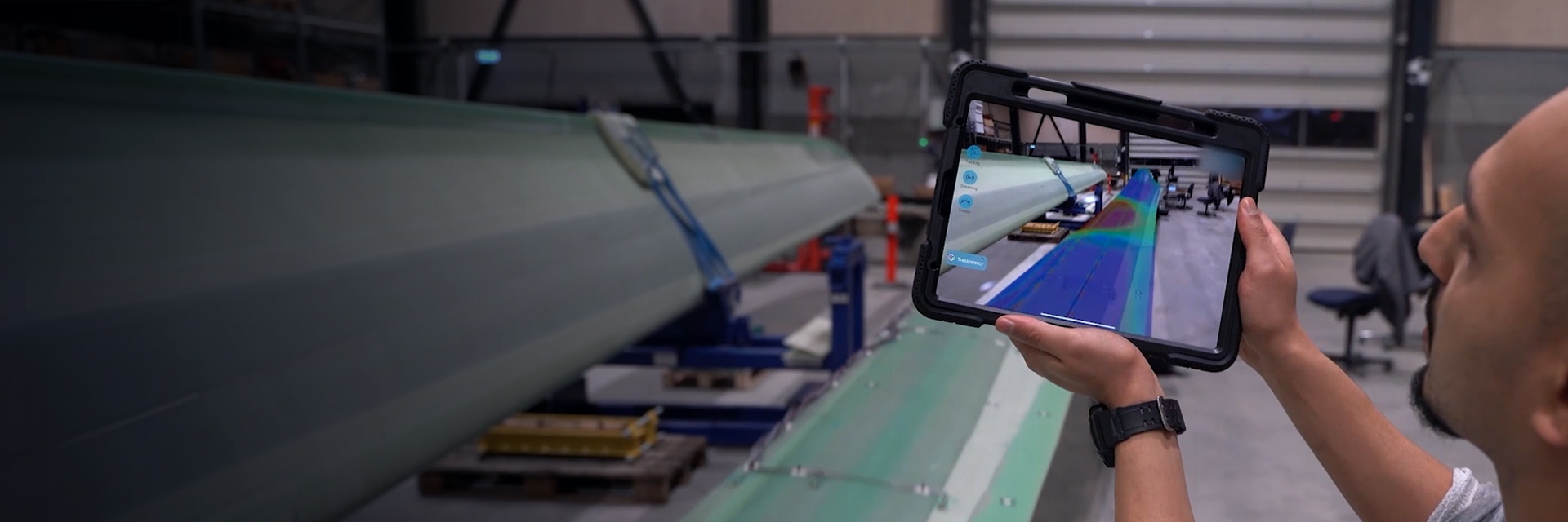 Ein Mann, der ein Tablet vor einem Industrieteil zeigt.