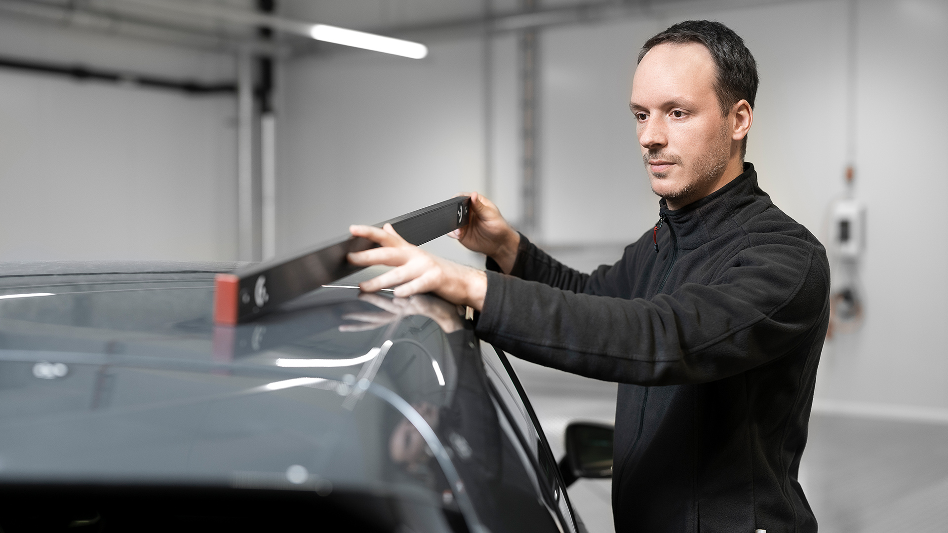 Ein Mann nutzt einen Längenmaßstab als Referenz, um eine Autokarosserie einzumessen.