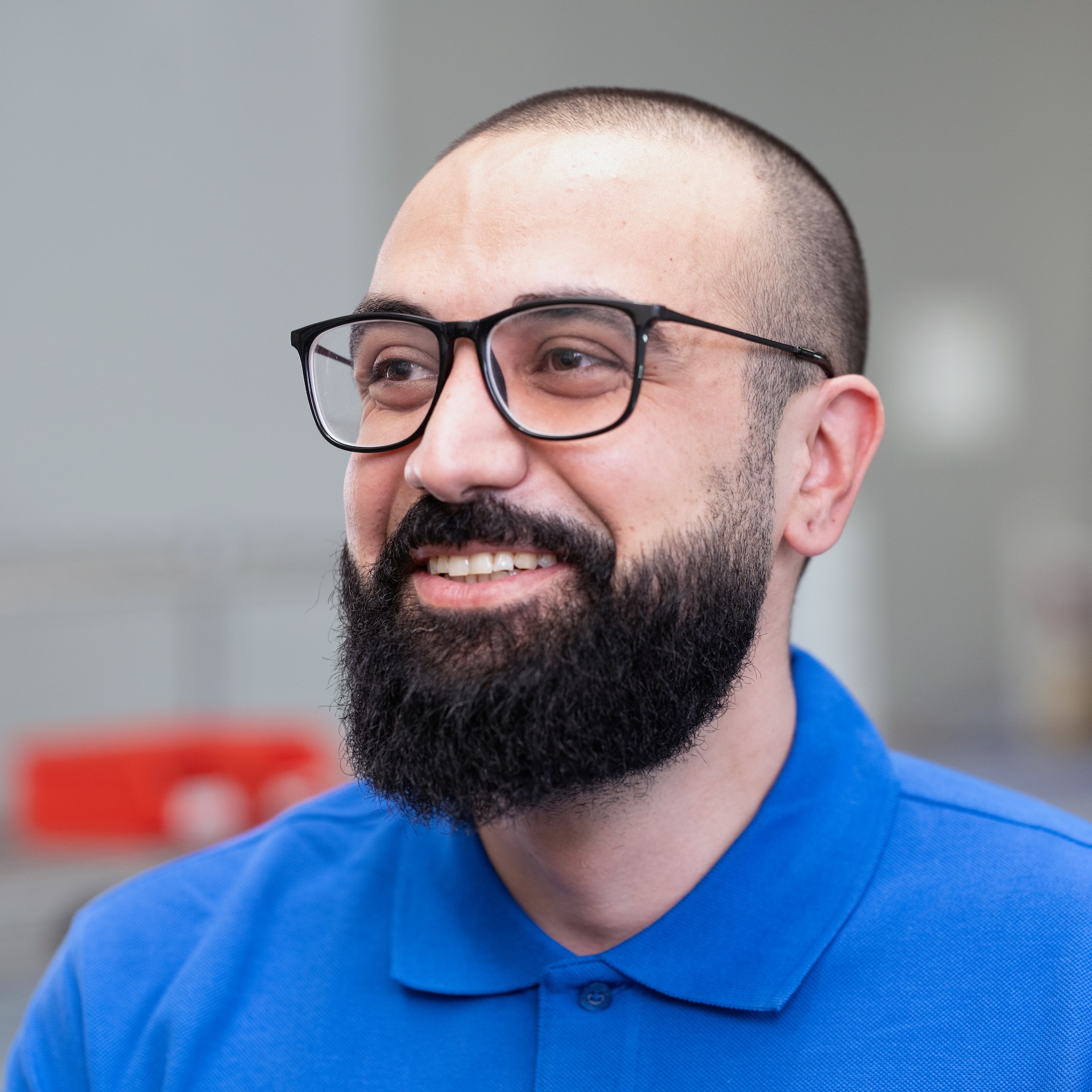 Ali El-Toufaili, ein bärtiger Mann mit Brille und blauem Poloshirt, lächelnd in einer hellen Halle.