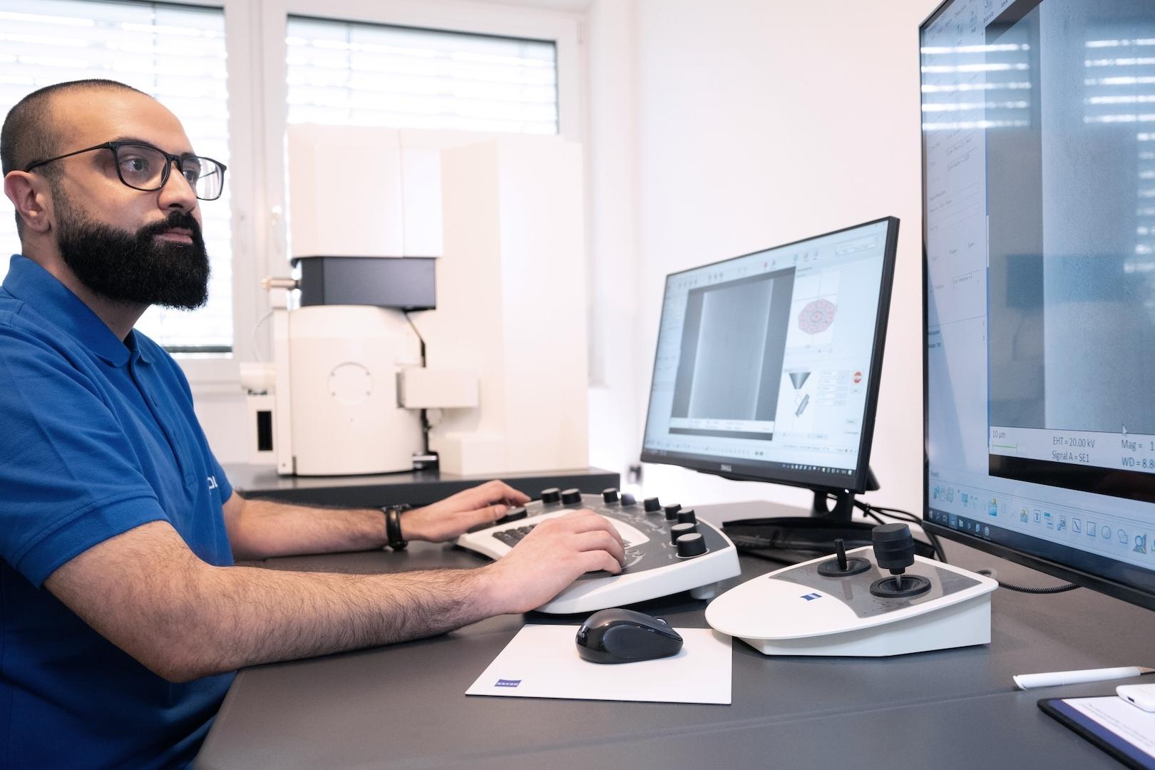 Ein Techniker bedient ein ZEISS Gerät und analysiert die Daten auf zwei Monitoren in einer modernen Laborumgebung.