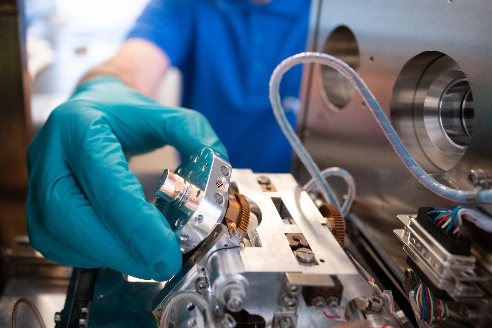 Eine behandschuhte Hand justiert ein Präzisionsbauteil im Inneren eines ZEISS EVO.