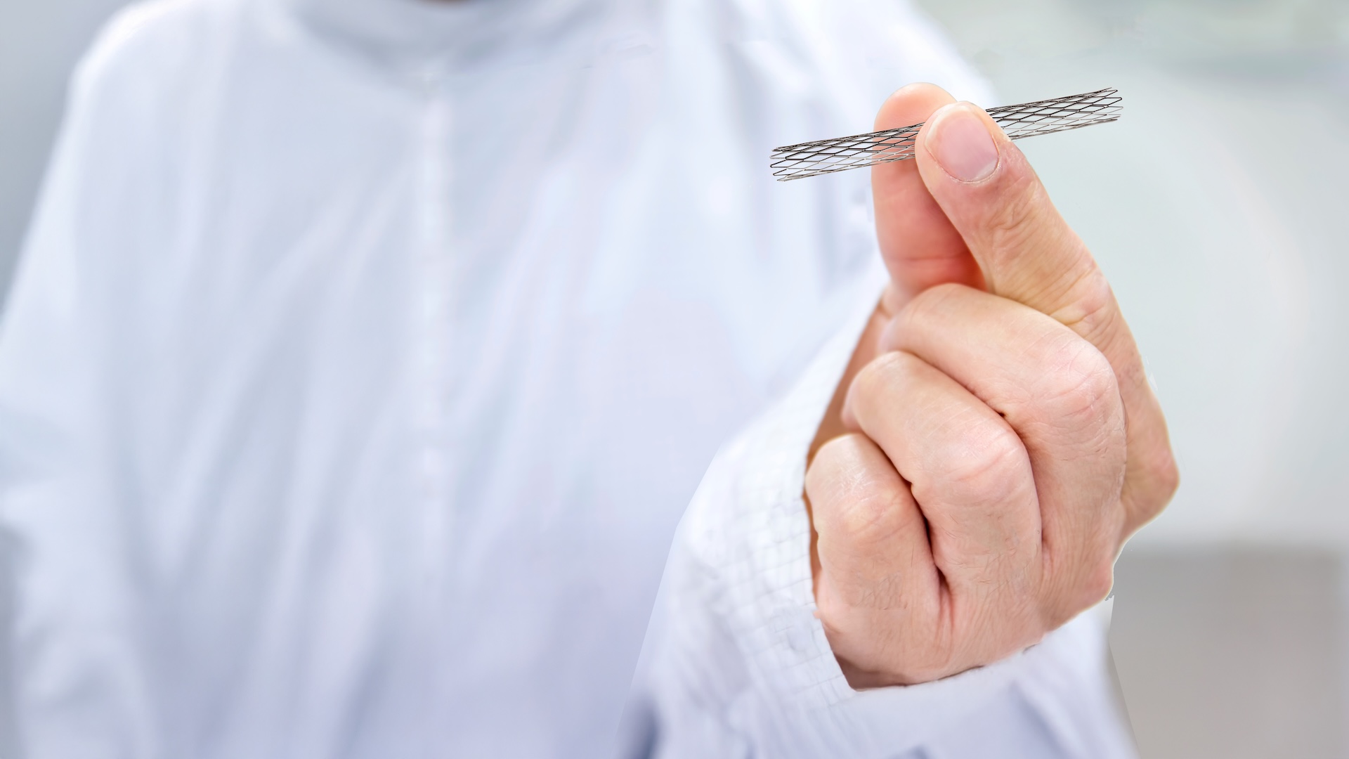  Eine Person in einem weißen Laborkittel hält in einer sauberen, klinischen Umgebung einen kleinen, zylindrischen medizinischen Stent zwischen ihren Fingern.
