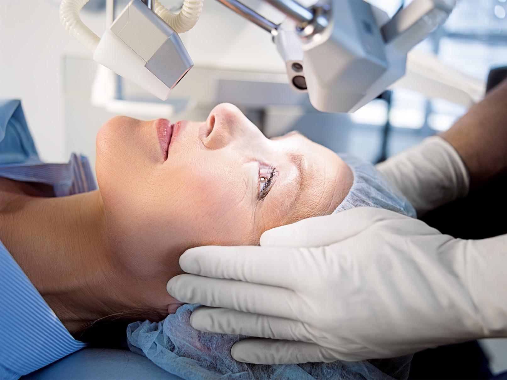 Ein Patient liegt unter einem medizinischen Bildgebungsgerät von ZEISS, während eine medizinische Fachkraft seinen Kopf während einer Augenuntersuchung oder einem chirurgischen Eingriff justiert.