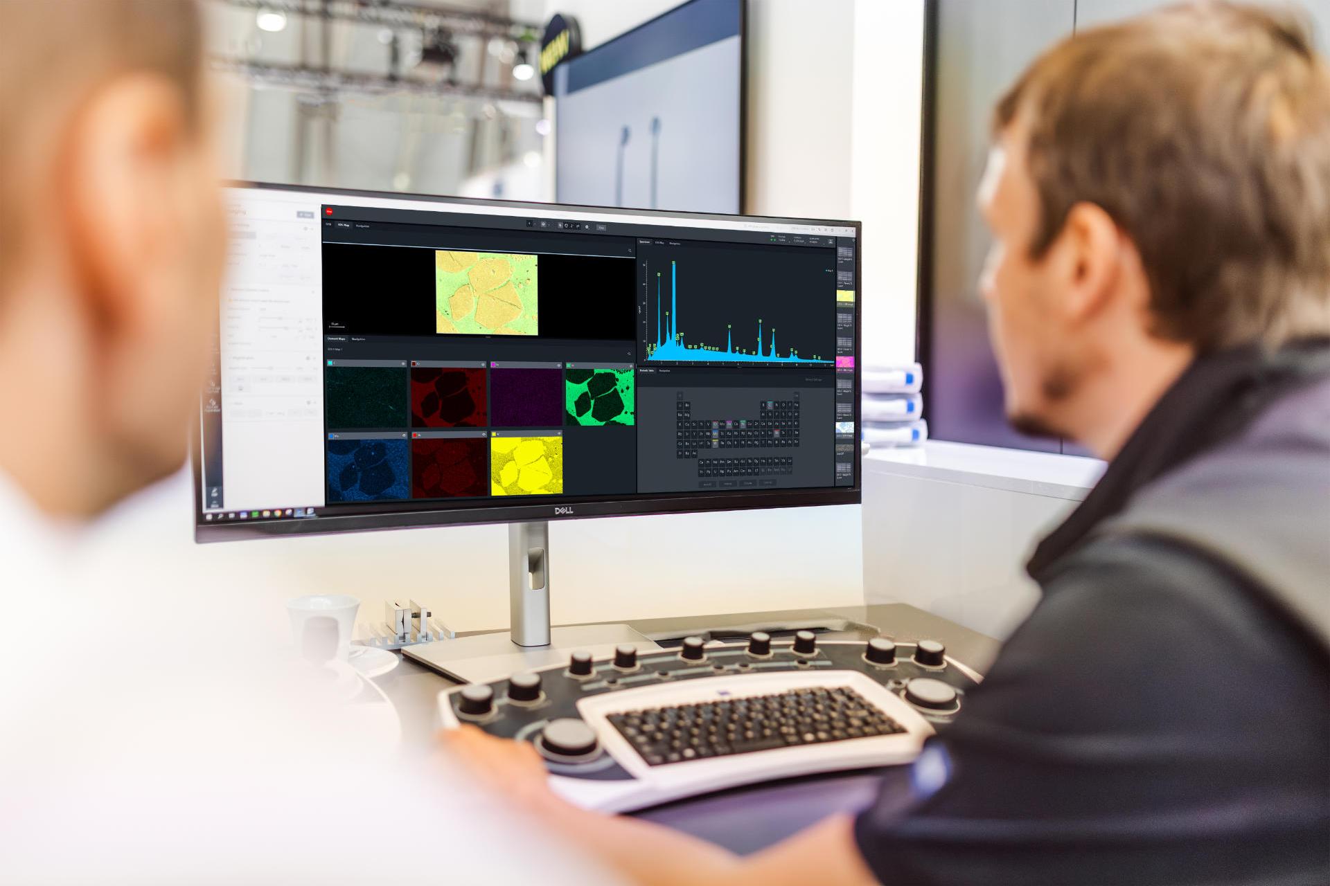 Zwei Menschen sitzen vor einem Monitor auf dem verschiedene Graphen und technische Darstellungen zu sehen sind