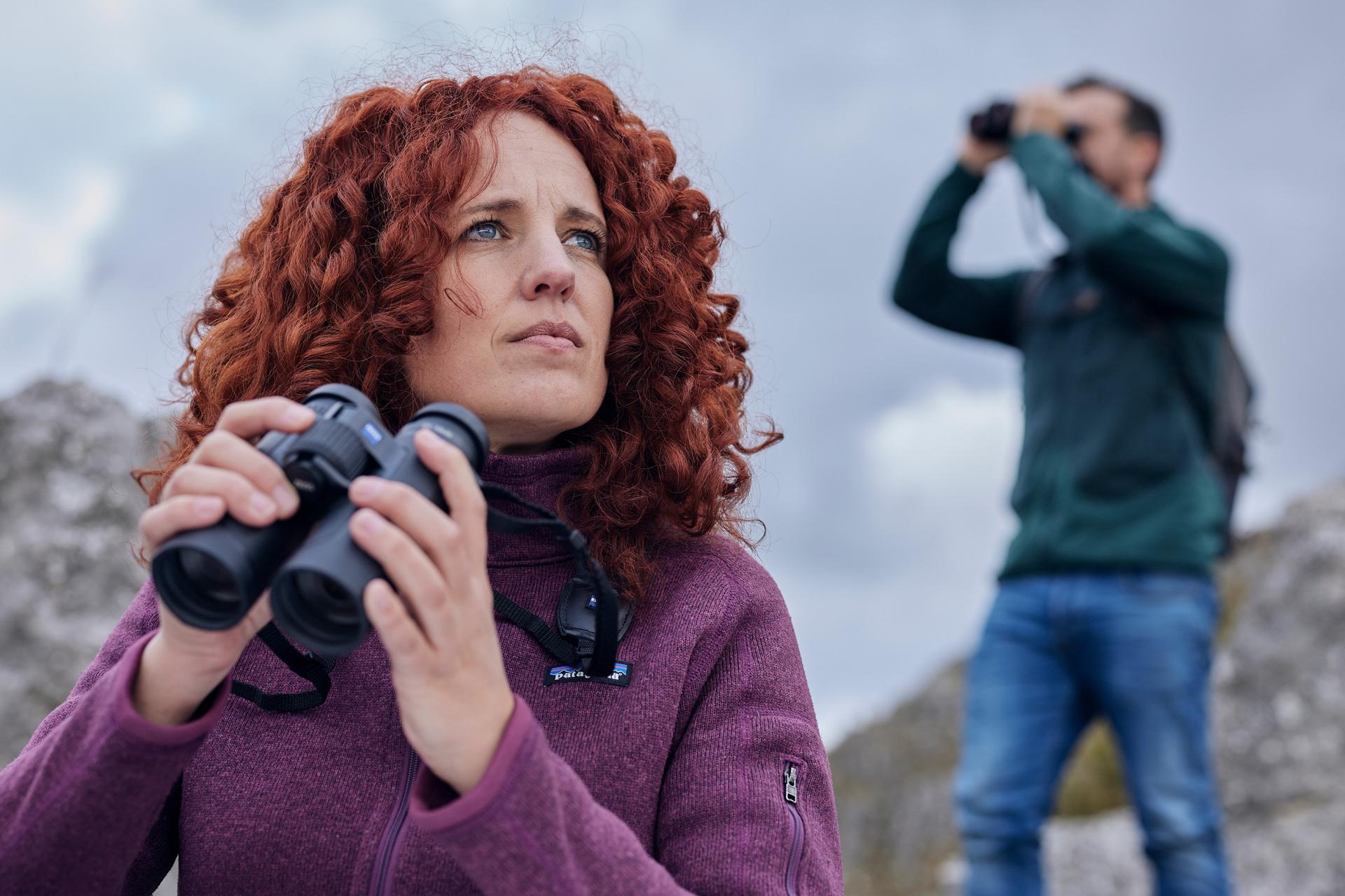 Zwei Personen im Freien mit einem Fernglas von ZEISS, eine Frau im Vordergrund und ein Mann, der im Hintergrund beobachtet.