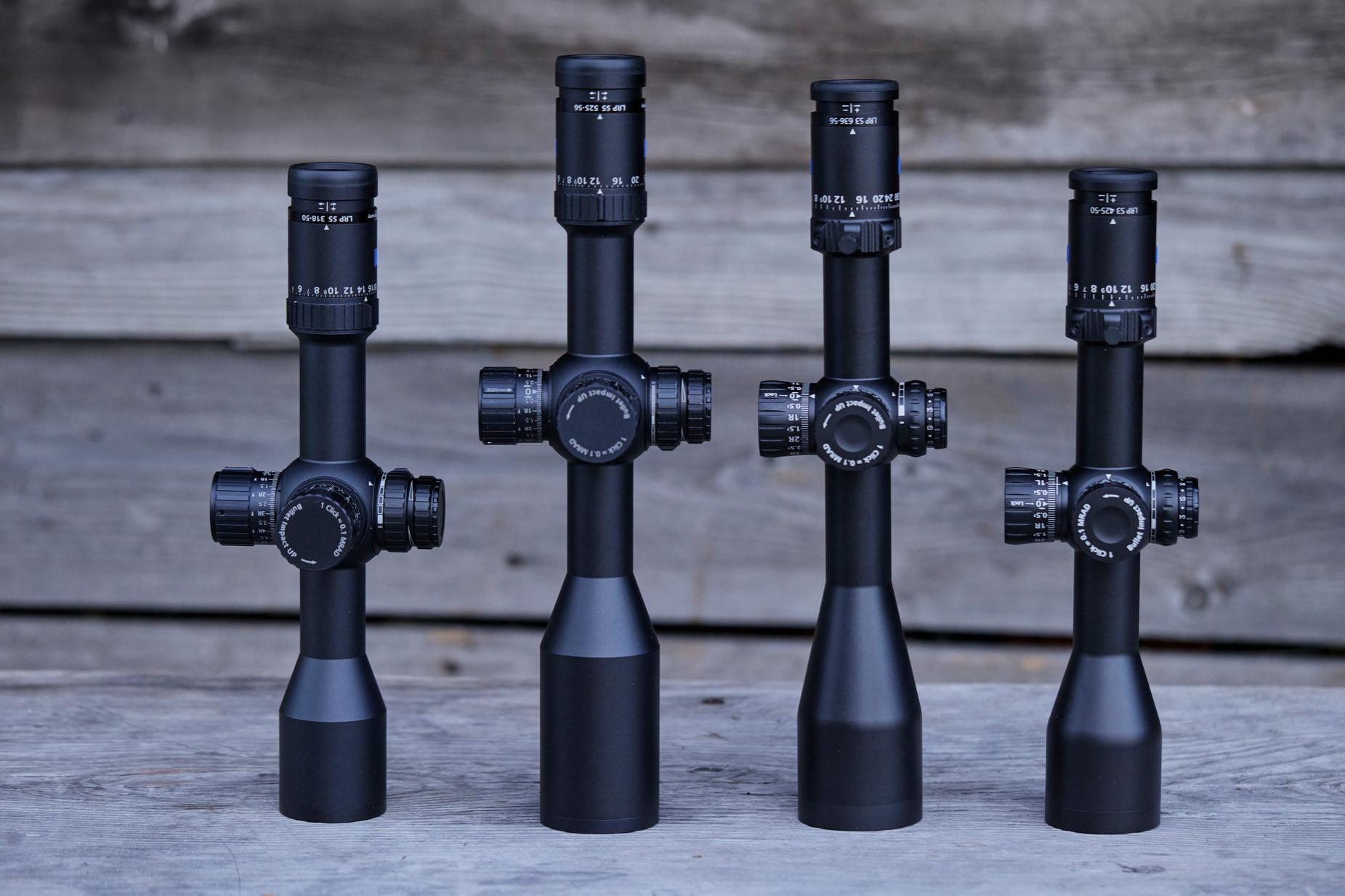 Vier ZEISS Zielfernrohre unterschiedlicher Größe sind aufrecht auf einer Holzoberfläche mit einem Holzhintergrund ausgestellt.