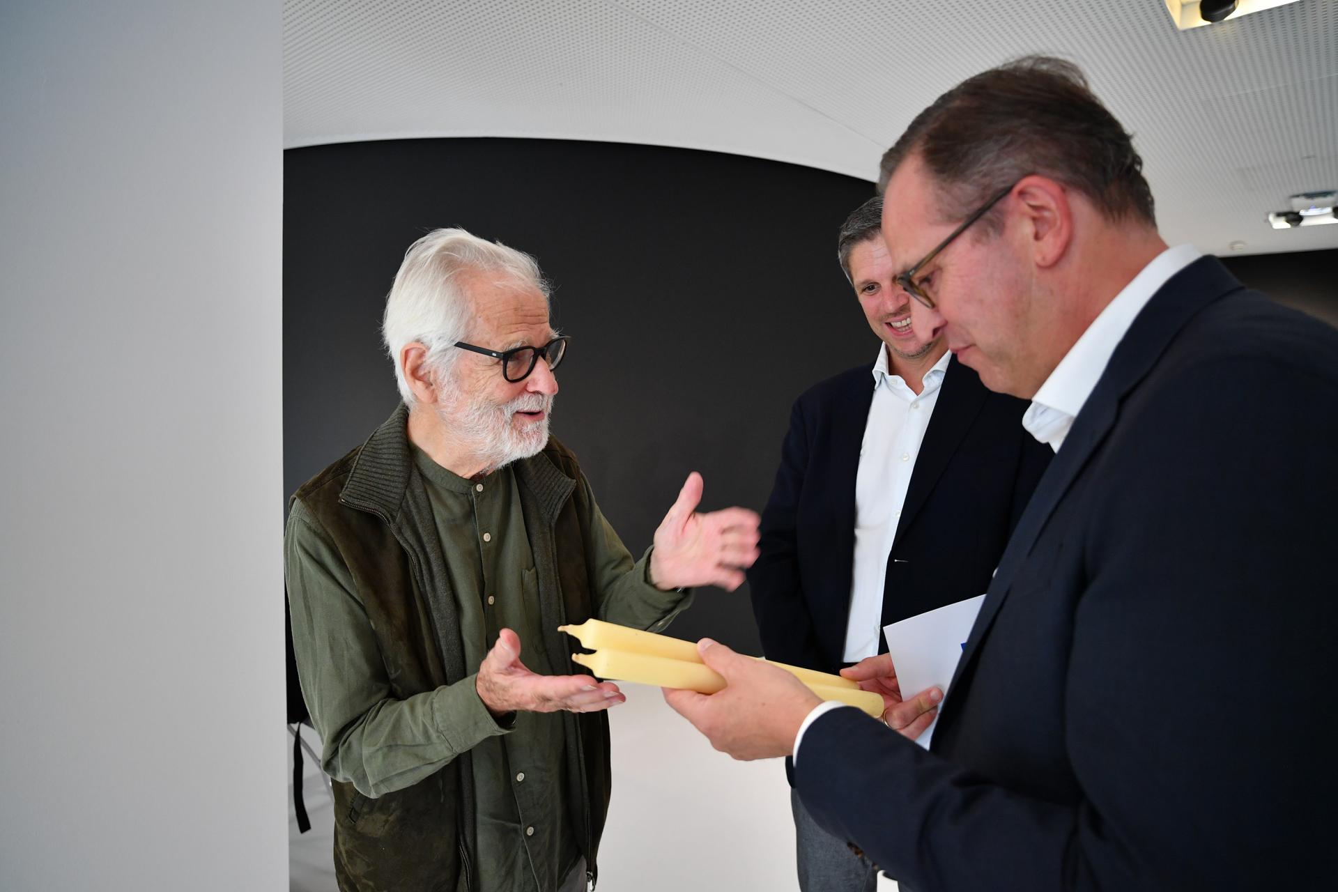 Drei Männer in Business-Kleidung diskutieren, während sie gelbe Kerzen begutachten.