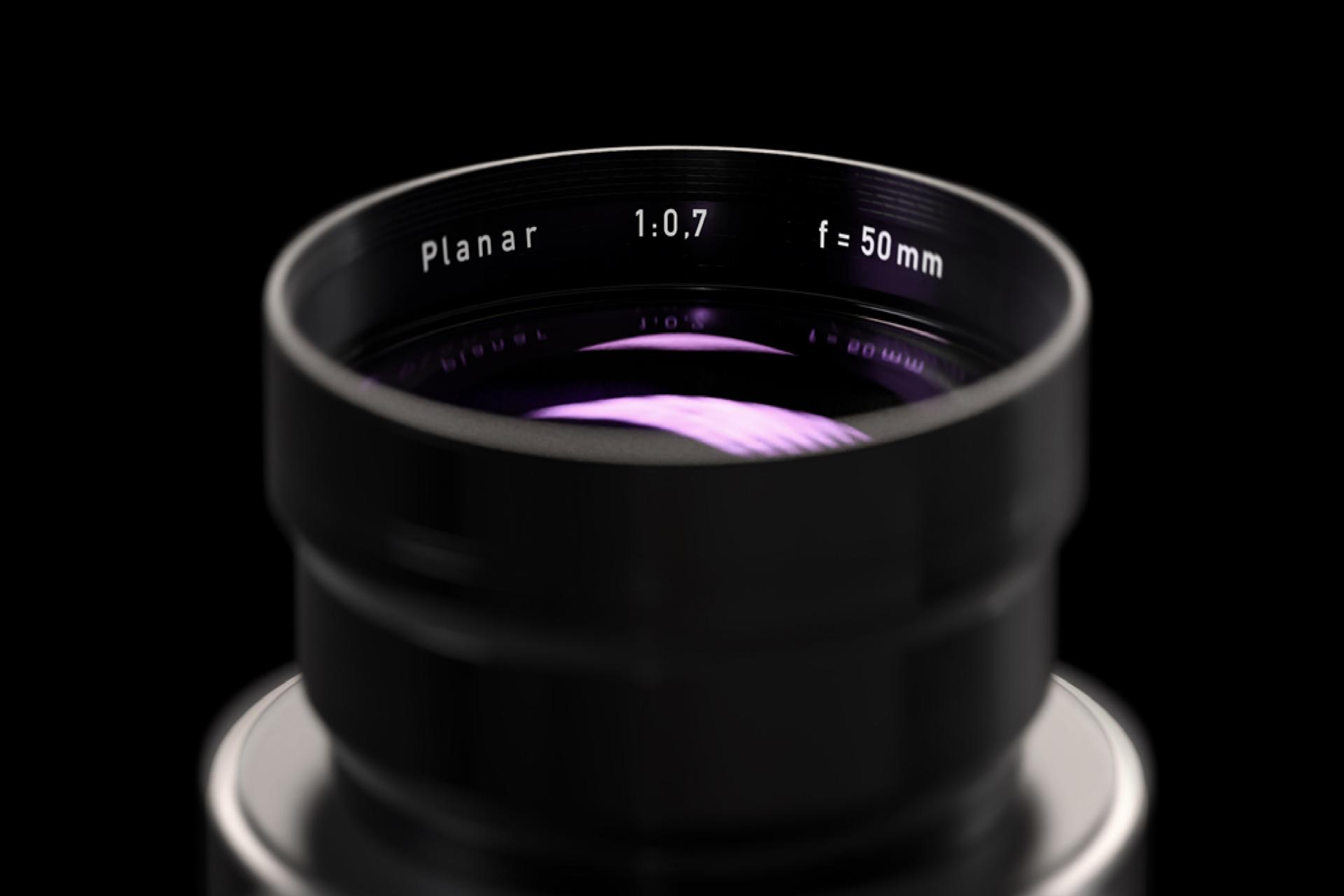 Nahaufnahme eines ZEISS Planar 50 mm f/0,7 Kameraobjektivs mit sichtbaren Glasreflexionen und eingravierten Spezifikationen.