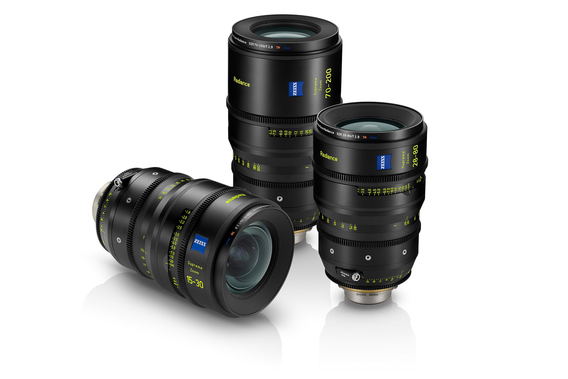Drei professionelle ZEISS-Kameraobjektive mit schwarzem Gehäuse und gelb-grünen Markierungen sind auf einer weißen reflektierenden Oberfläche ausgestellt.