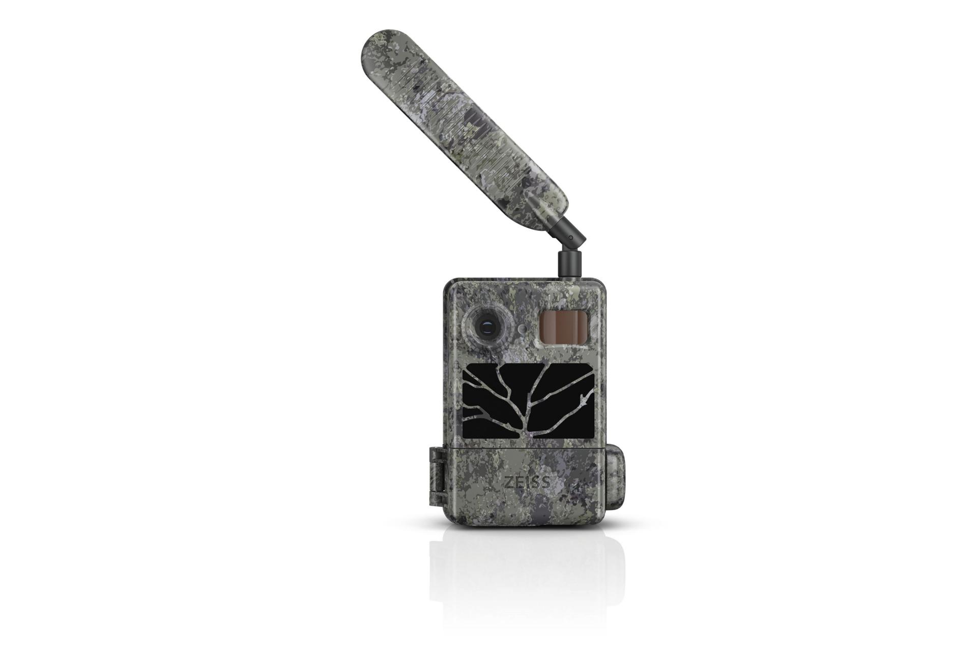 Getarnte ZEISS-Wildkamera mit verlängerter Antenne, Objektiv, Sensoren und einem Display, das ein Schwarz-Weiß-Bild von Ästen zeigt.