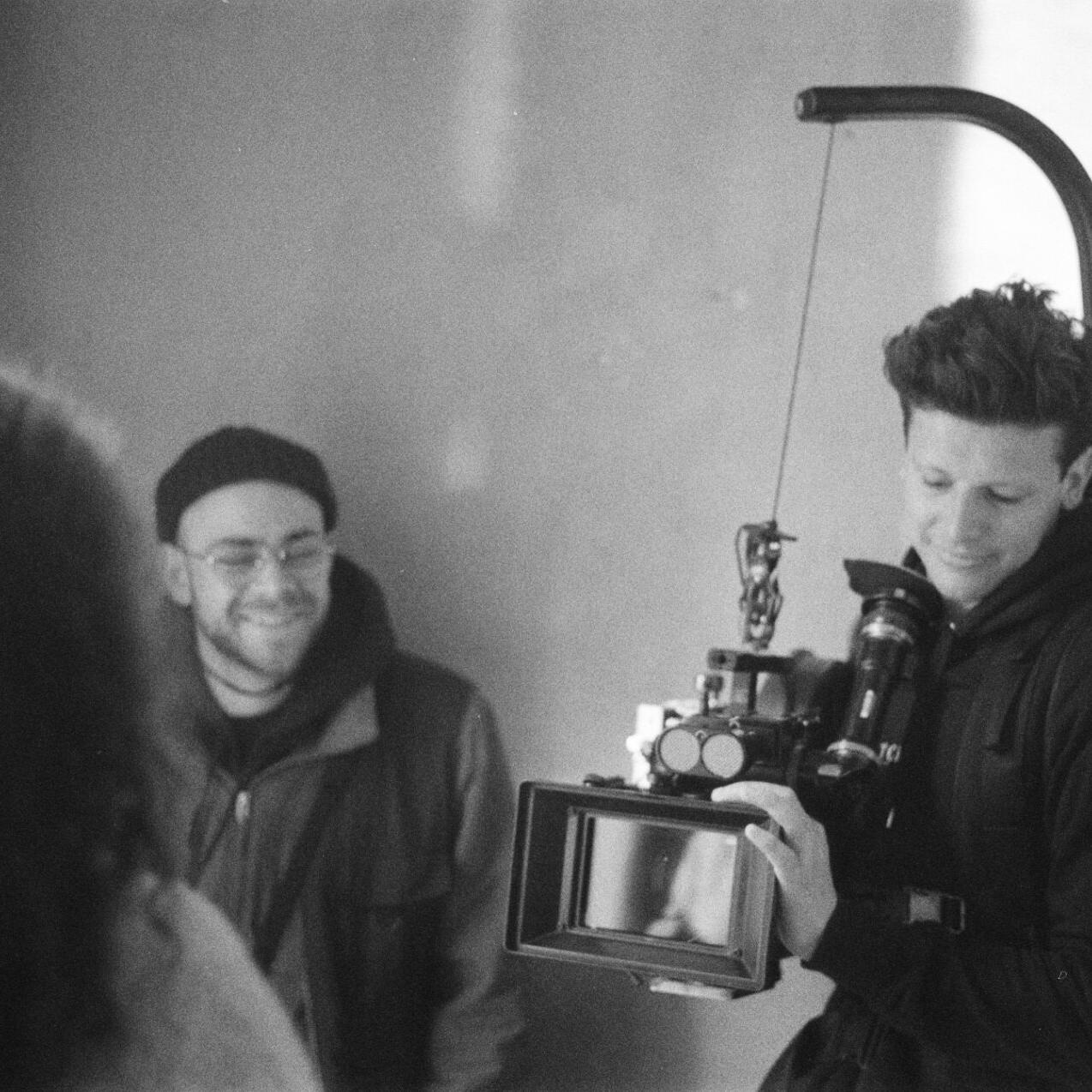 A person operates a professional camera rig equipped with a ZEISS lens, while others observe and engage in conversation.