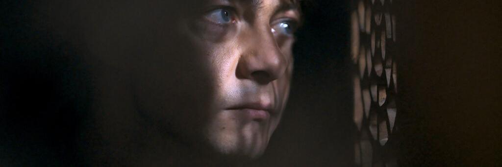 A close-up of a man's face partially illuminated by patterned light through a screen, showcasing ZEISS lens precision in capturing fine detail and contrast.