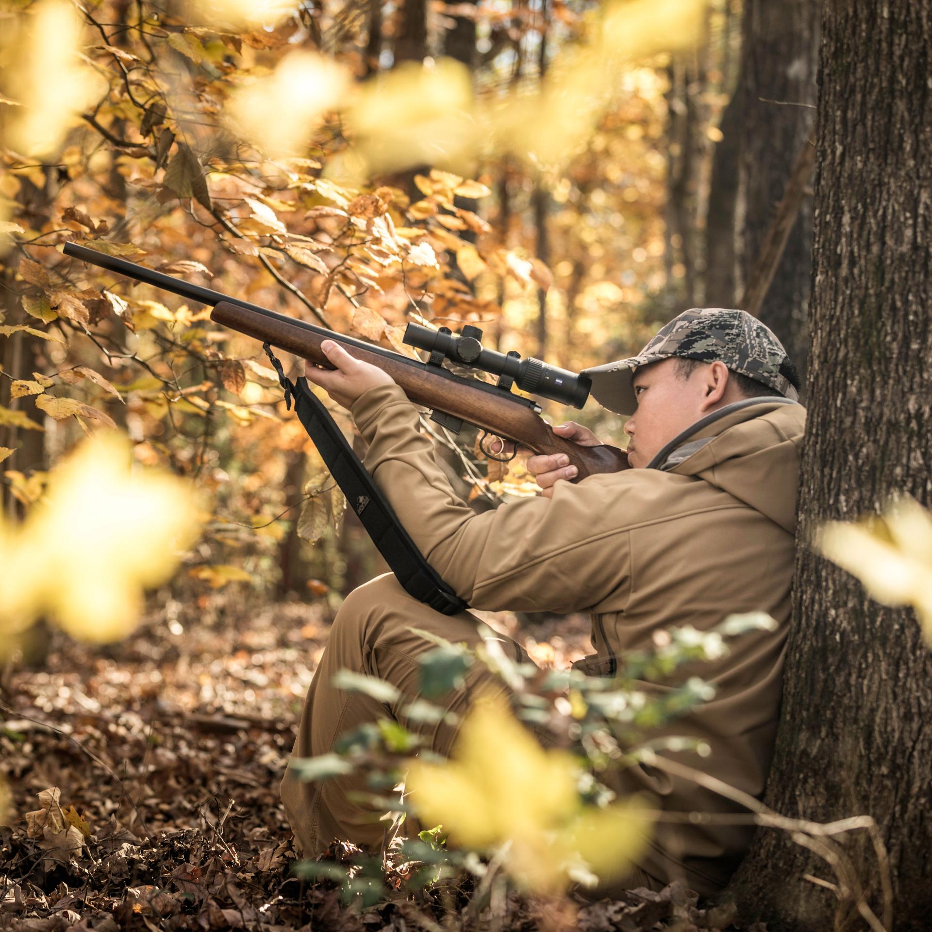 Hunter aiming his rifle equipped with a ZEISS Conquest V4 1-4x24 riflescope in a forest, designed for fast target acquisition in short-range hunting