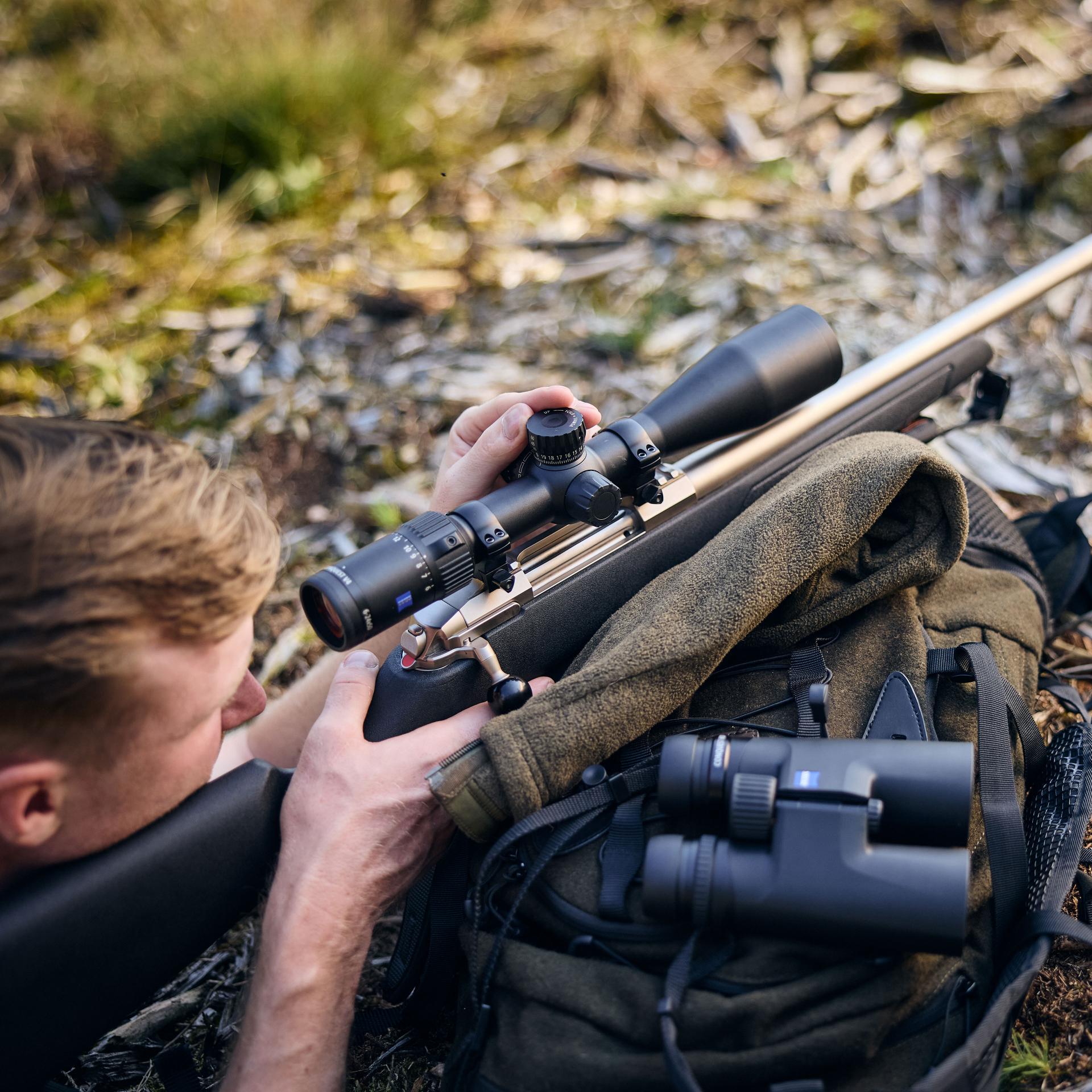Hunter lying prone with a rifle mounted with a ZEISS Conquest V4 6-24x50 riflescope, designed for precision long-range hunting.