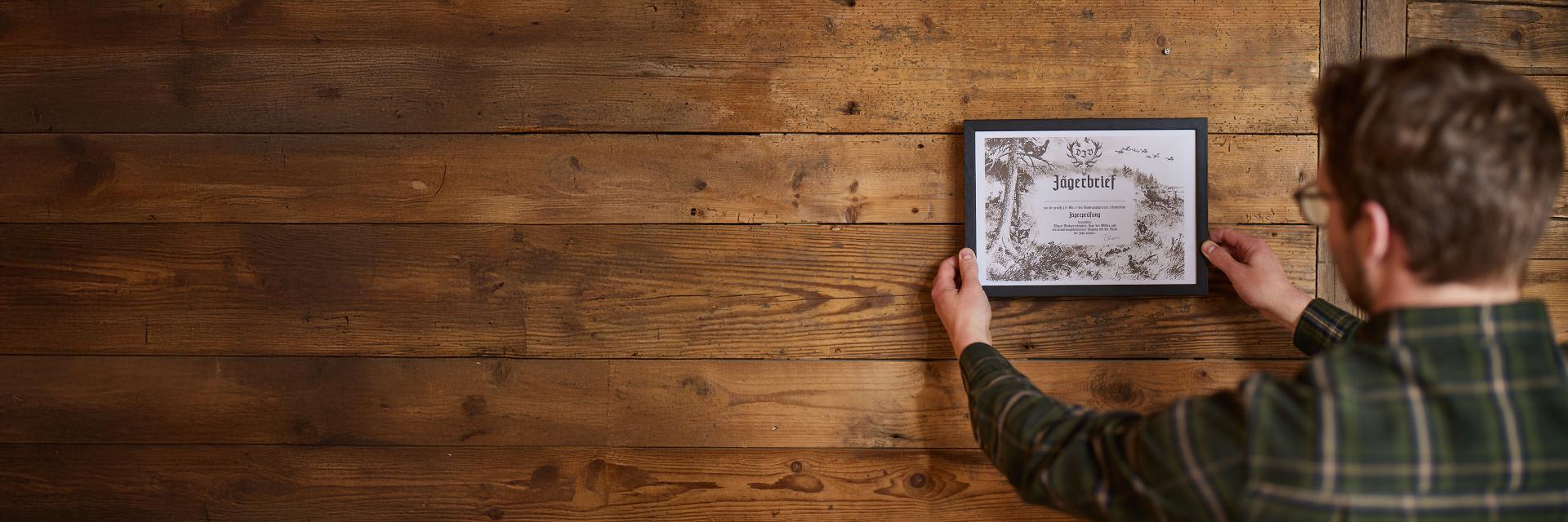 Eine lächelnde Frau erhält bei einer Zeremonie im Freien, umgeben von anderen Teilnehmern in ZEISS-Jagdbekleidung, mit einem Handschlag ihr Jägerbrief-Zertifikat.
