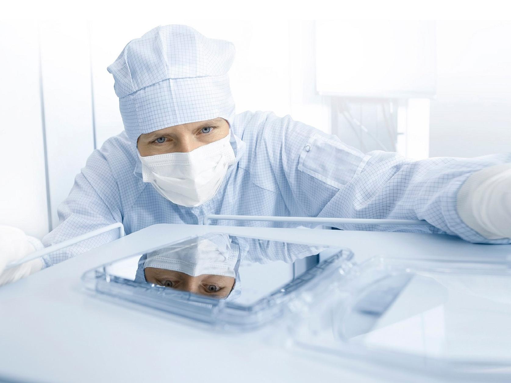 Ein Mitarbeiter arbeitet mit Reinraumanzug an der Perfektion einer Photomaske.