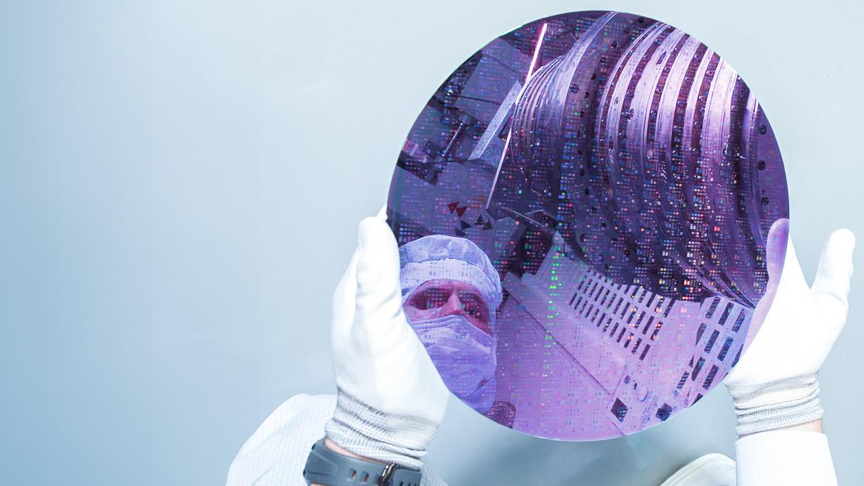 Ein ZEISS SMT Mitarbeiter hält, die für die DUV-Technologie wichtige Komponente in Form einer dünnen scheibenförmigen Siliziumscheibe – den sogenannten Wafer – in der Hand.
