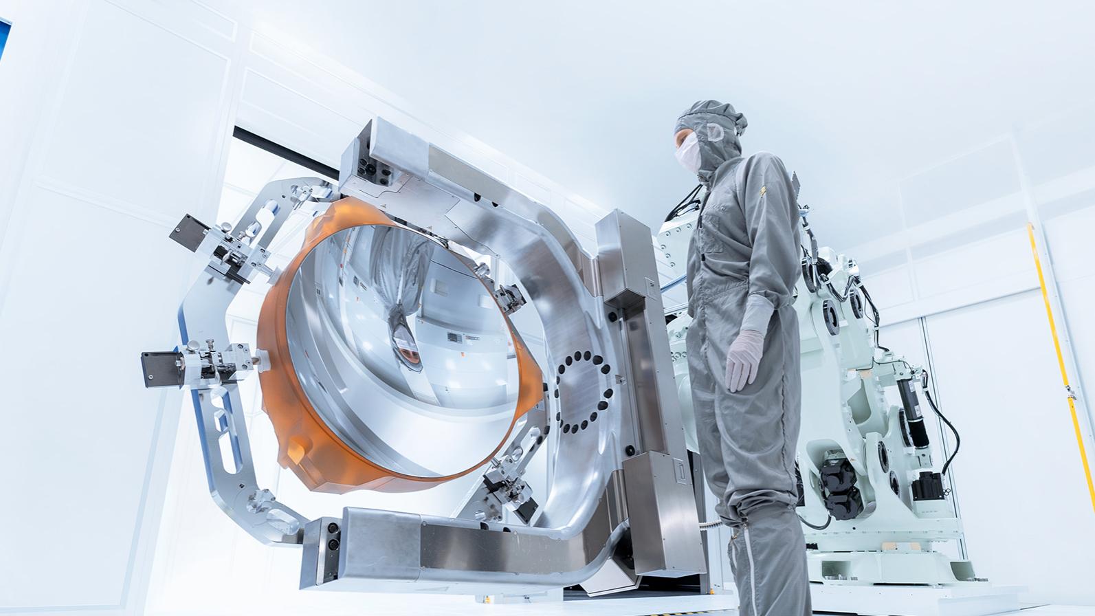 Ein Mitarbeiter blickt auf den beschichteten Spiegel der High-NA-EUV-Lithographie im Reinraum der ZEISS Semiconductor Manufacturing Technology