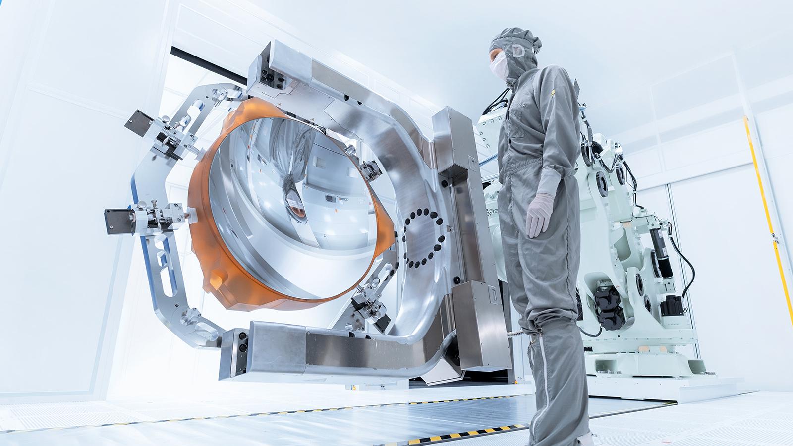 Ein Mitarbeiter blickt auf den beschichteten Spiegel der High-NA-EUV-Lithographie im Reinraum der ZEISS Semiconductor Manufacturing Technology