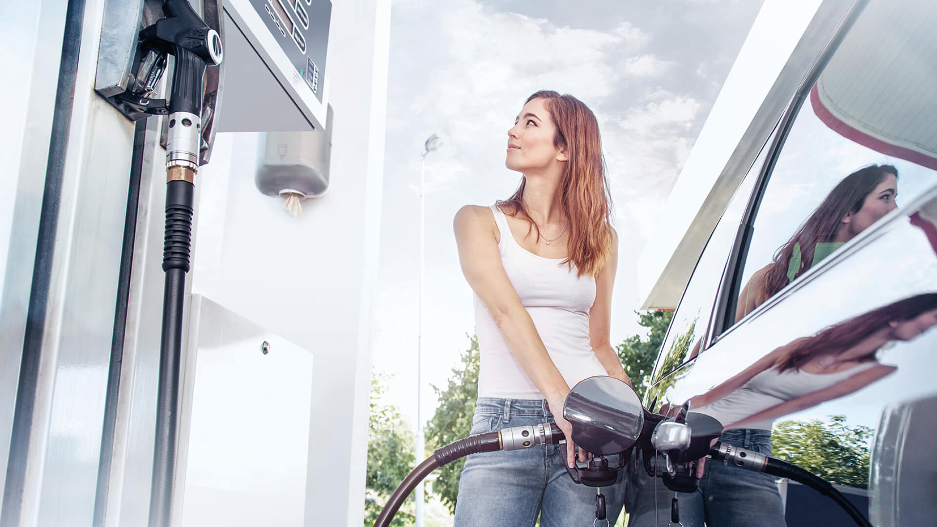 junge Frau steht an der Zapfsäule einer Tankstelle und betankt ihr Fahrzeug mit Ethanol auf Maisbasis