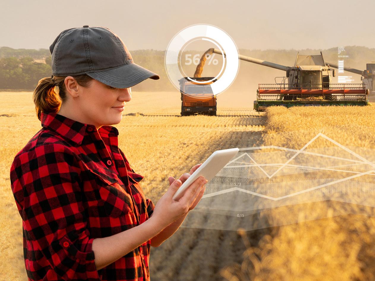 Landwirtin mit Tablet vor Erntemaschinen