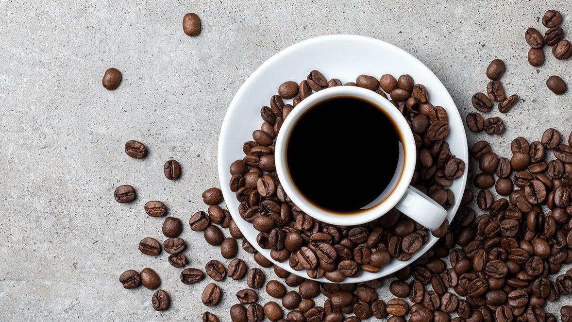 Tasse Kaffee mit Kaffeebohnen auf Betontisch