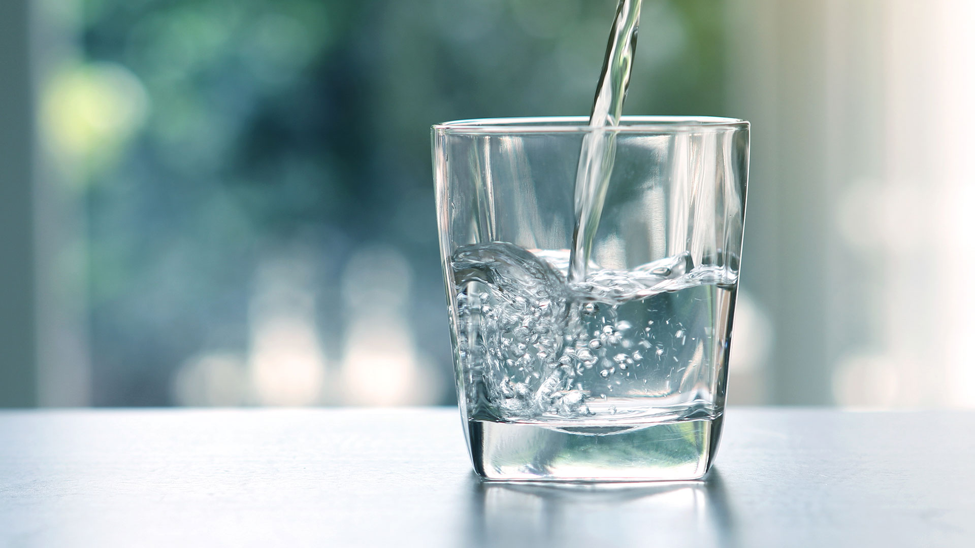 Nahaufnahme des Ausgießens von sauberem Trinkwasser aus einer Flasche auf dem Wohnzimmertisch