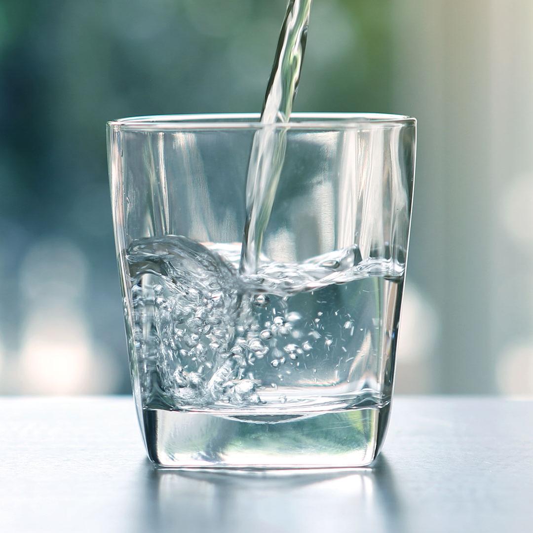 Nahaufnahme des Ausgießens von gereinigtem Trinkwasser aus einer Flasche auf dem Wohnzimmertisch