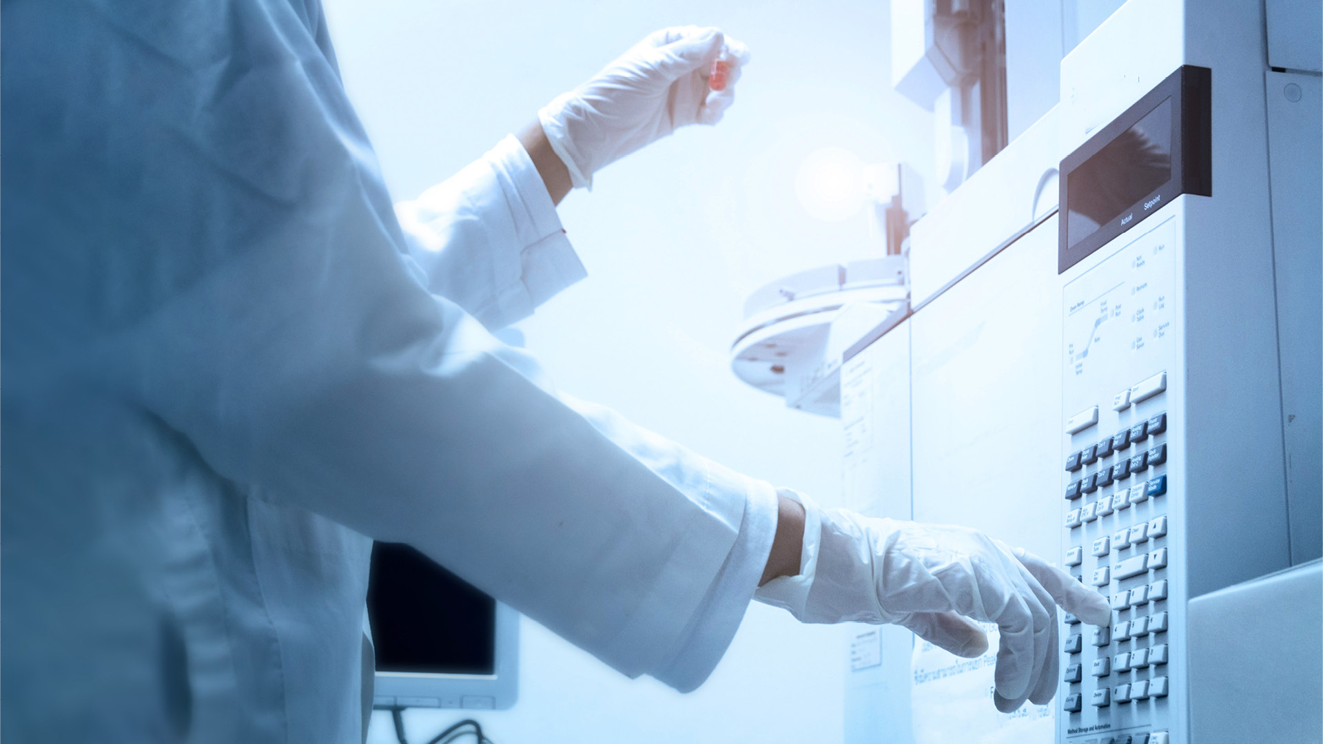 Ein Wissenschaftler hält ein bernsteinfarbenes Fläschchen in der Hand und drückt den Kontrollknopf der GC-Chromatographie.