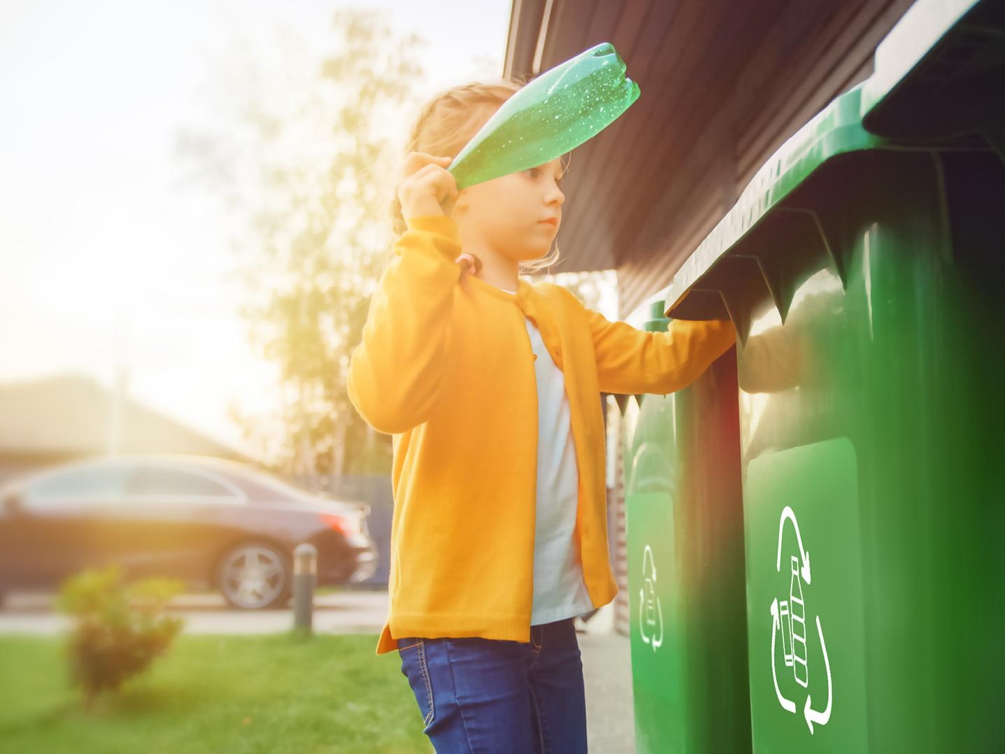 Junges Mädchen wirft eine leere Plastikflasche in einen Mülleimer. Sie benutzt den richtigen Mülleimer. Recycling