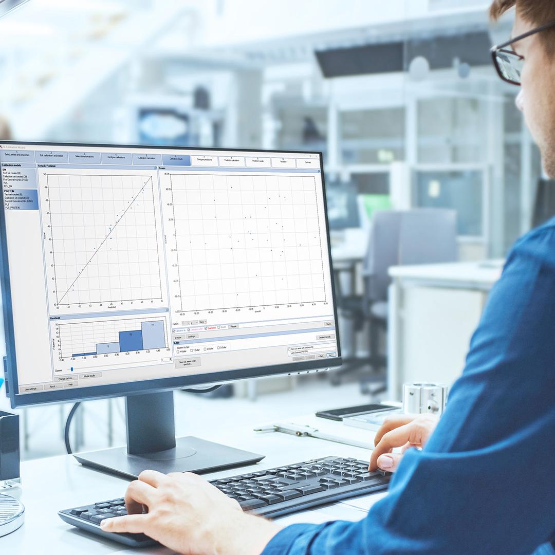 Blick über die Schulter eines Ingenieurs, der mit SensoLogic Software auf einem Computer arbeitet. Im Hintergrund technische Anlage mit Industriedesign