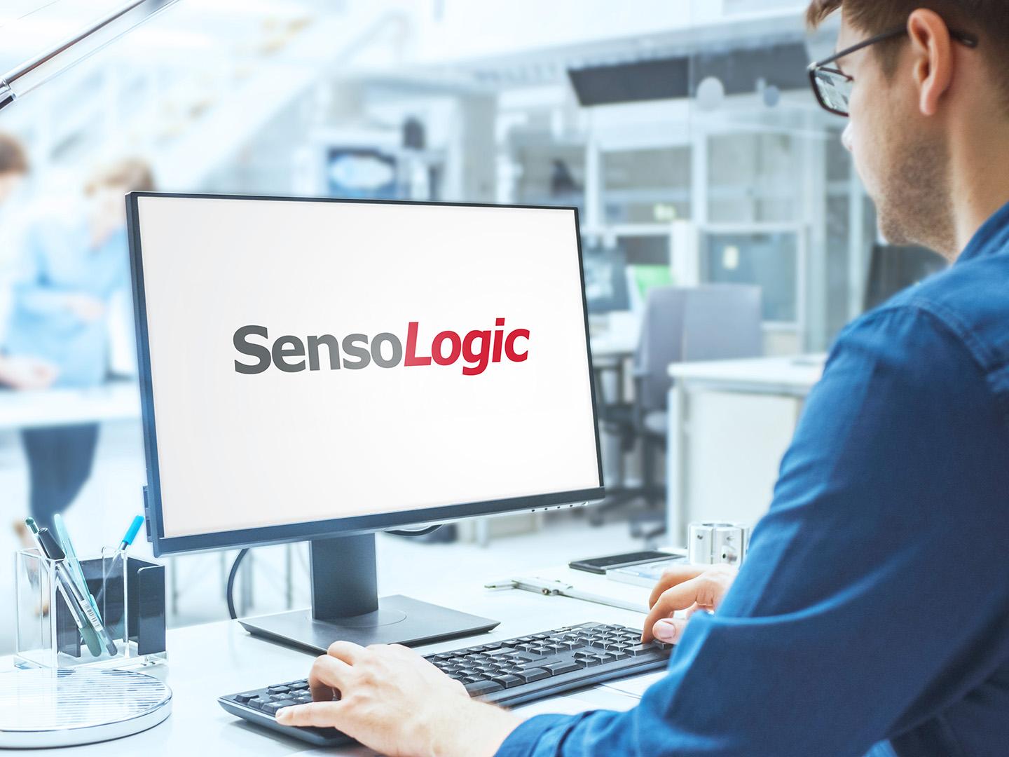 Over the shoulder shot of engineer working with SensoLogic software on screen desktop computer. In the background engineering facility with industrial design